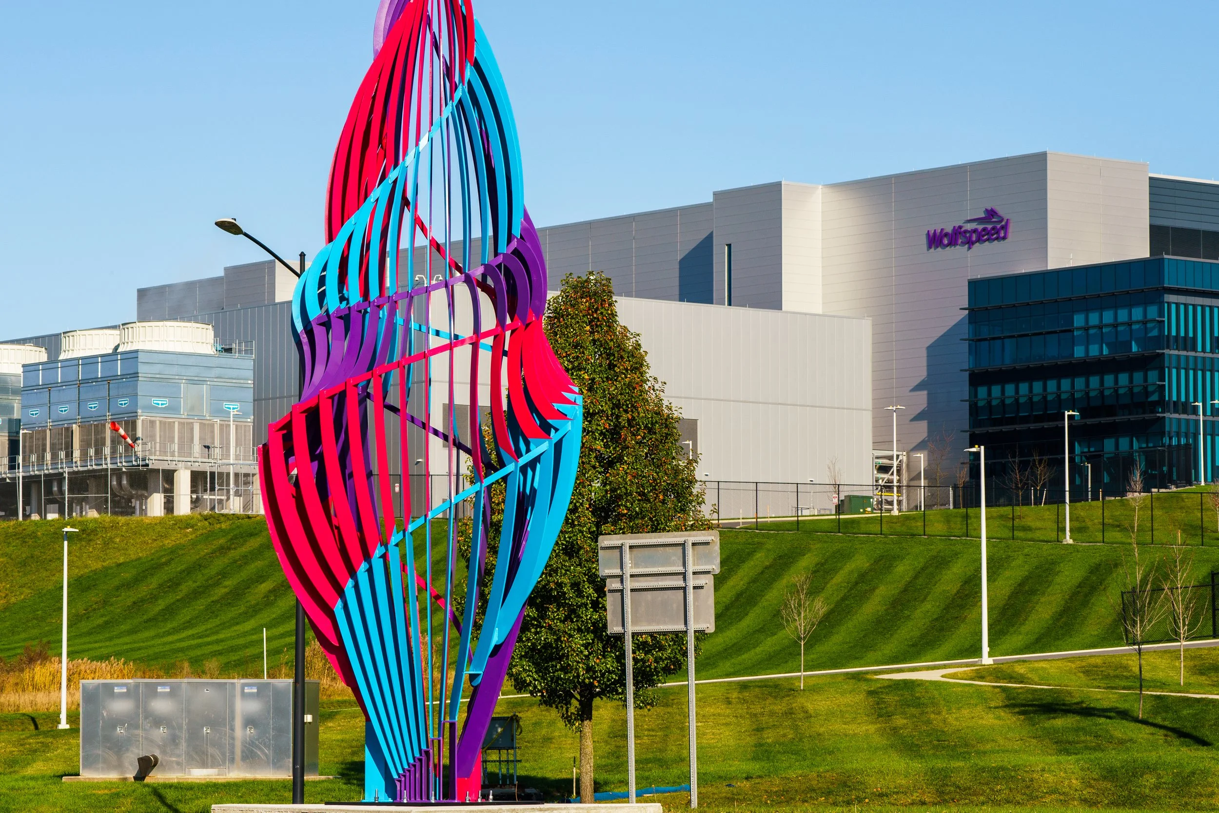 Colorful abstract sculpture in front of a large building with the 'Wolfspeed' logo, surrounded by a grassy area and trees under a clear blue sky.