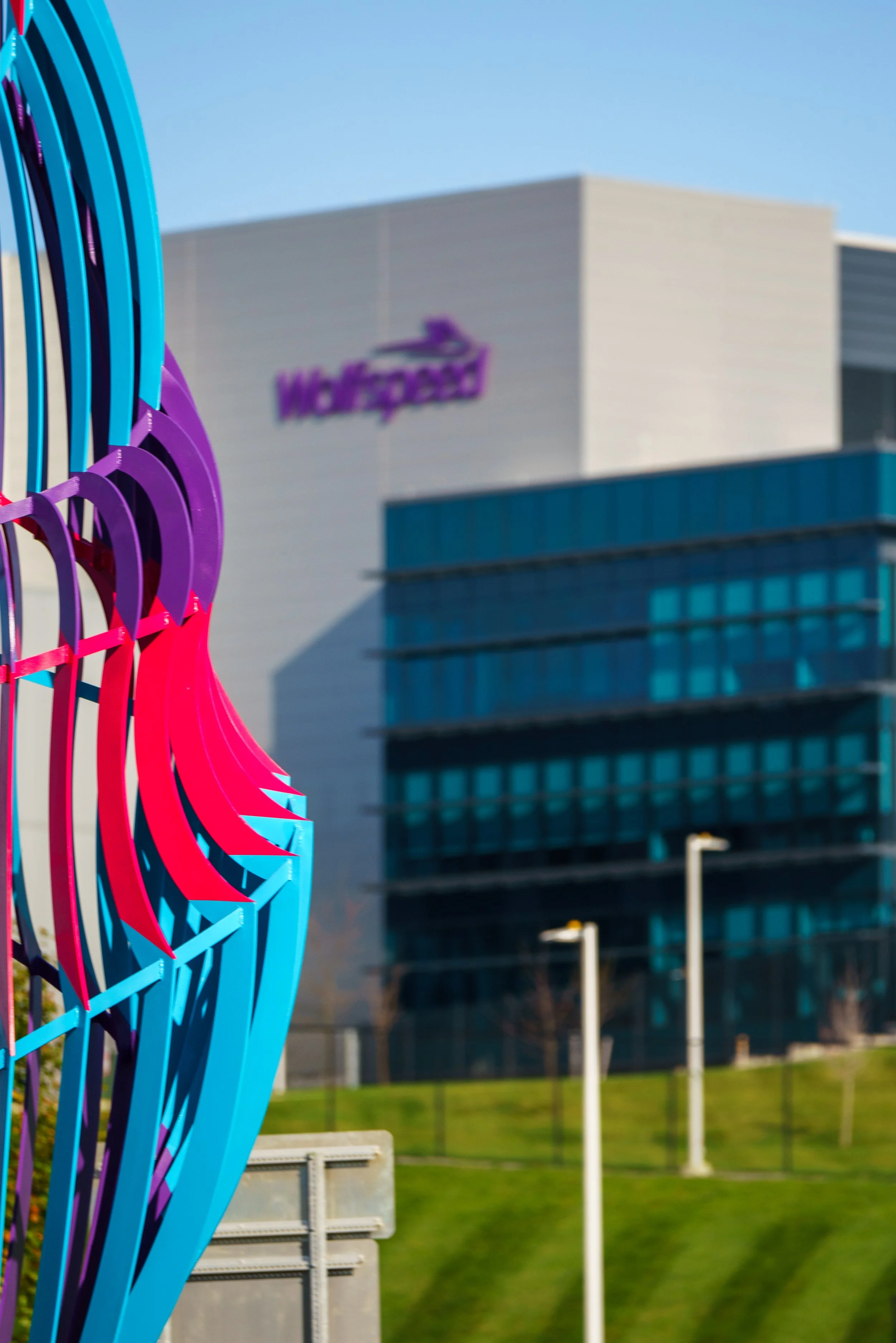 Colorful modern sculpture with curved blue and pink elements in front of a corporate building with the 'Wells Fargo' logo.
