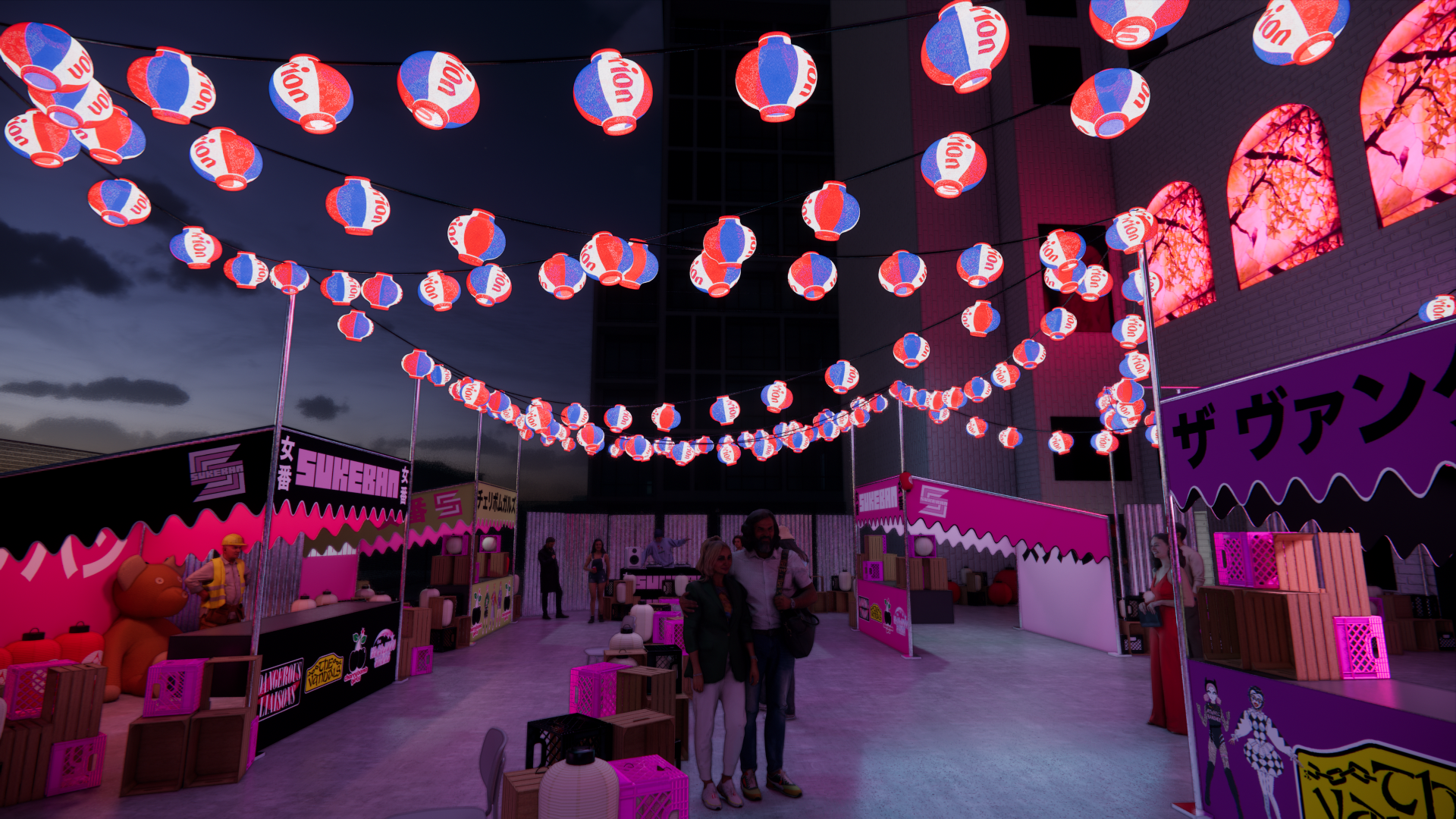 Outdoor scene at night with hanging red, white, and blue lanterns and pink booths, featuring people walking around at a festival or event.