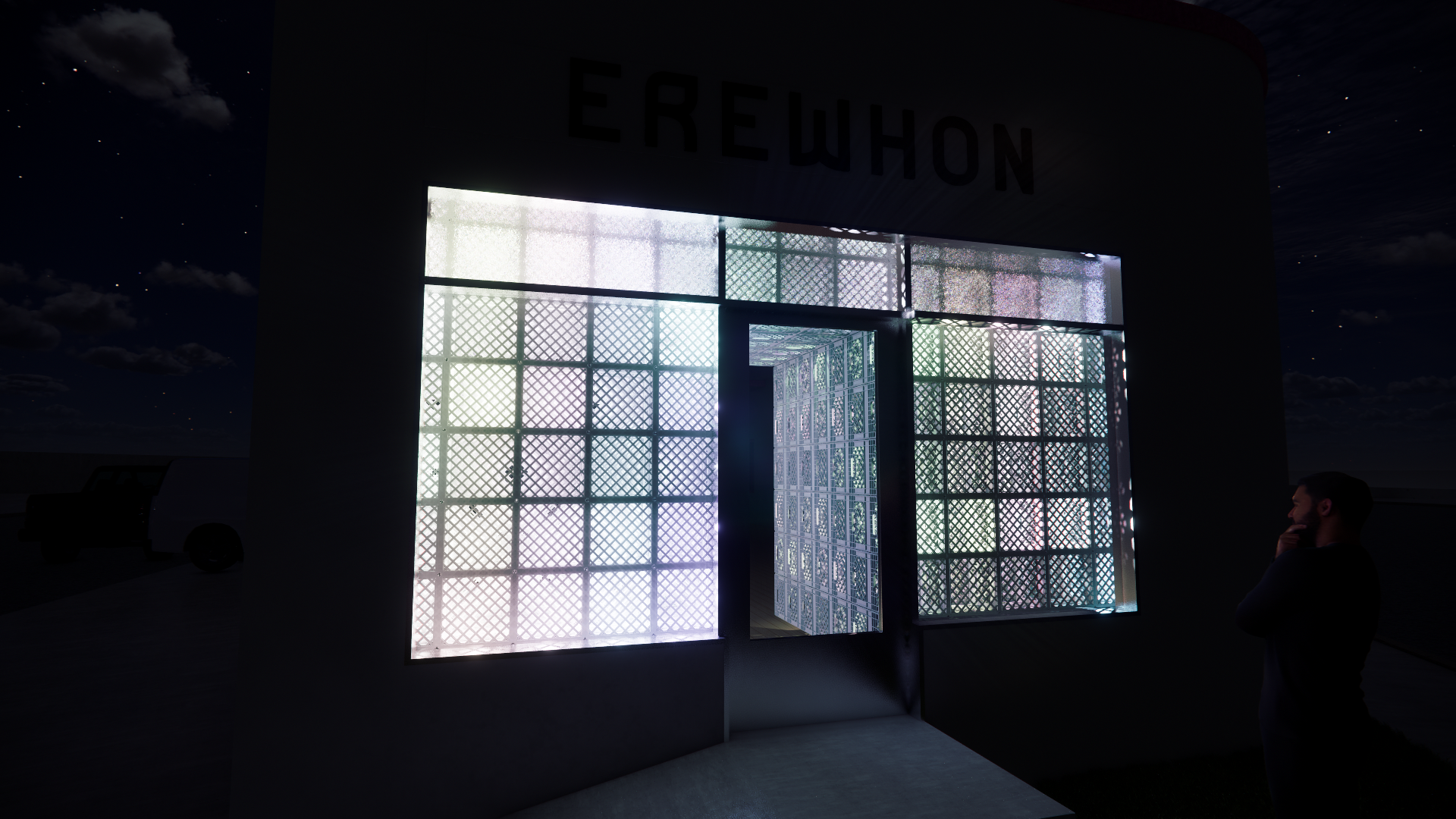 Nighttime view of a building with a colorful illuminated decorative facade made of lattice panels, and a man standing nearby with his hand on his chin.