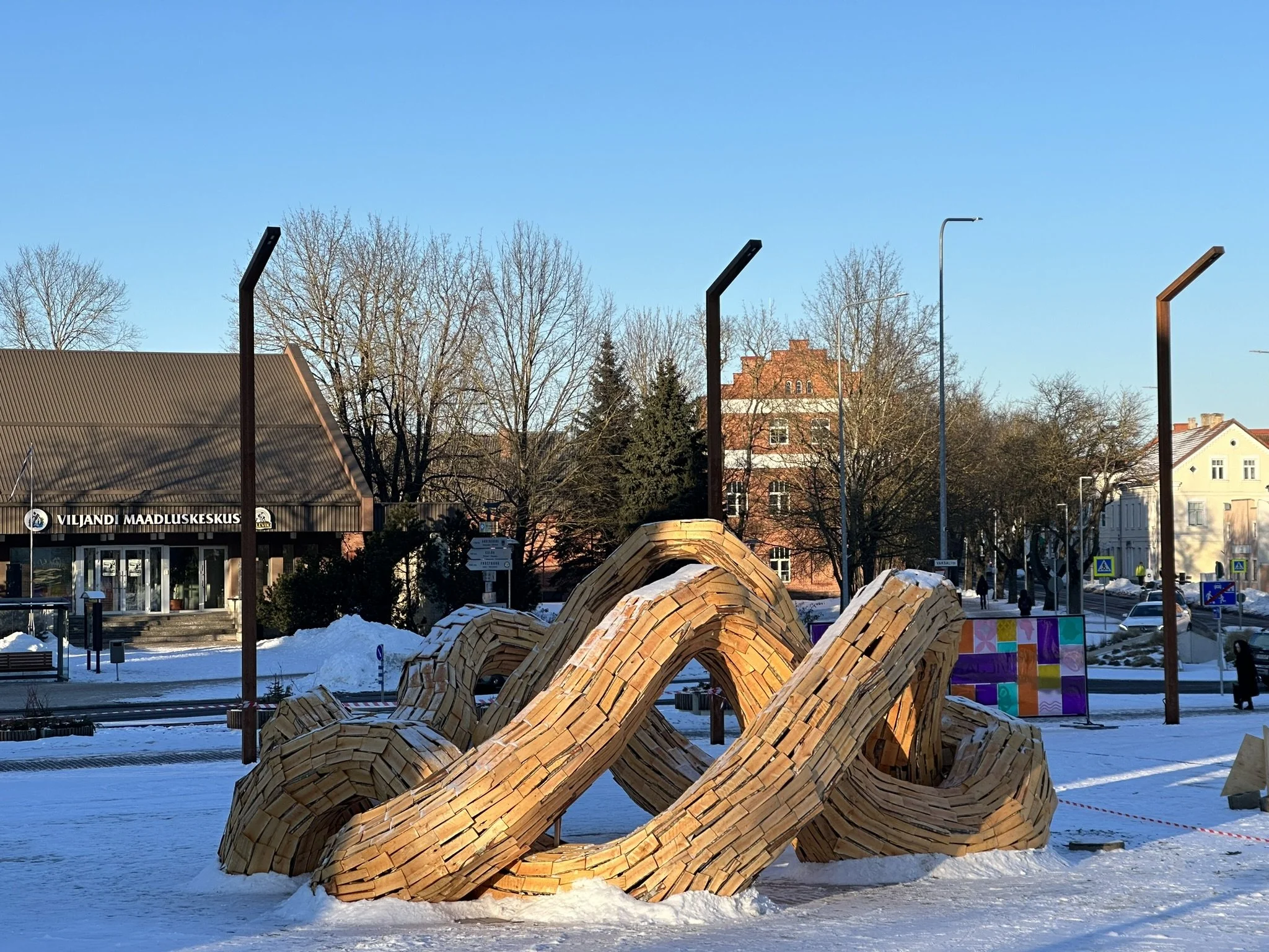 A large wooden sculpture resembling a playful ladybug with six rounded body segments, situated outdoors in a snow-covered area during winter.
