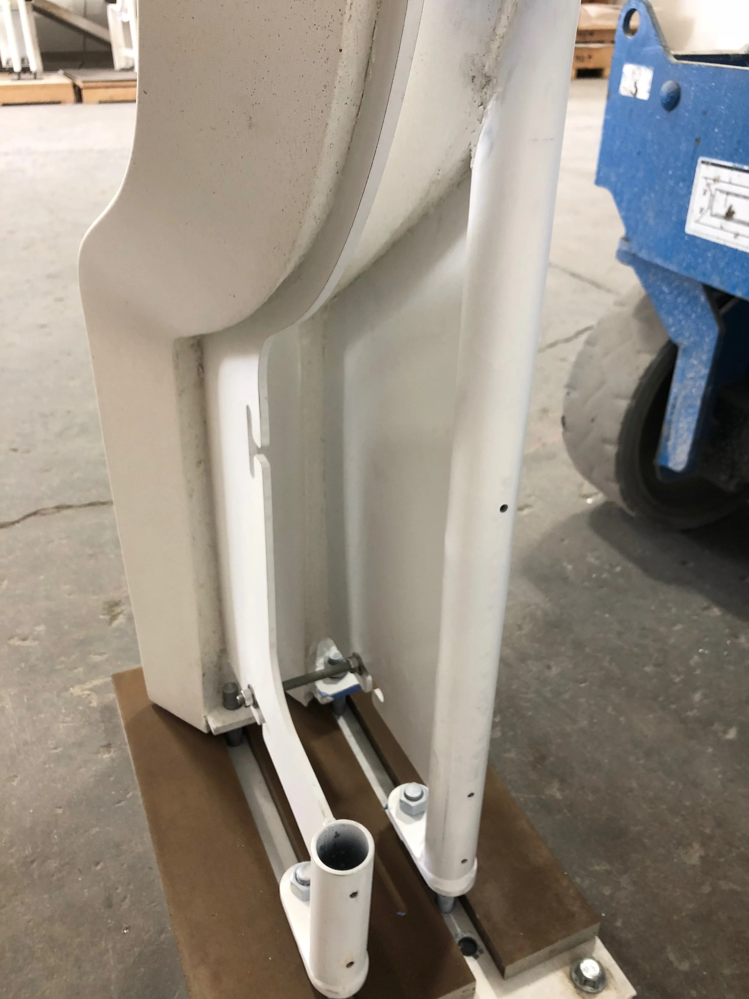 Close-up of white metal pipes and brackets mounted on a brown base in an industrial or warehouse setting.