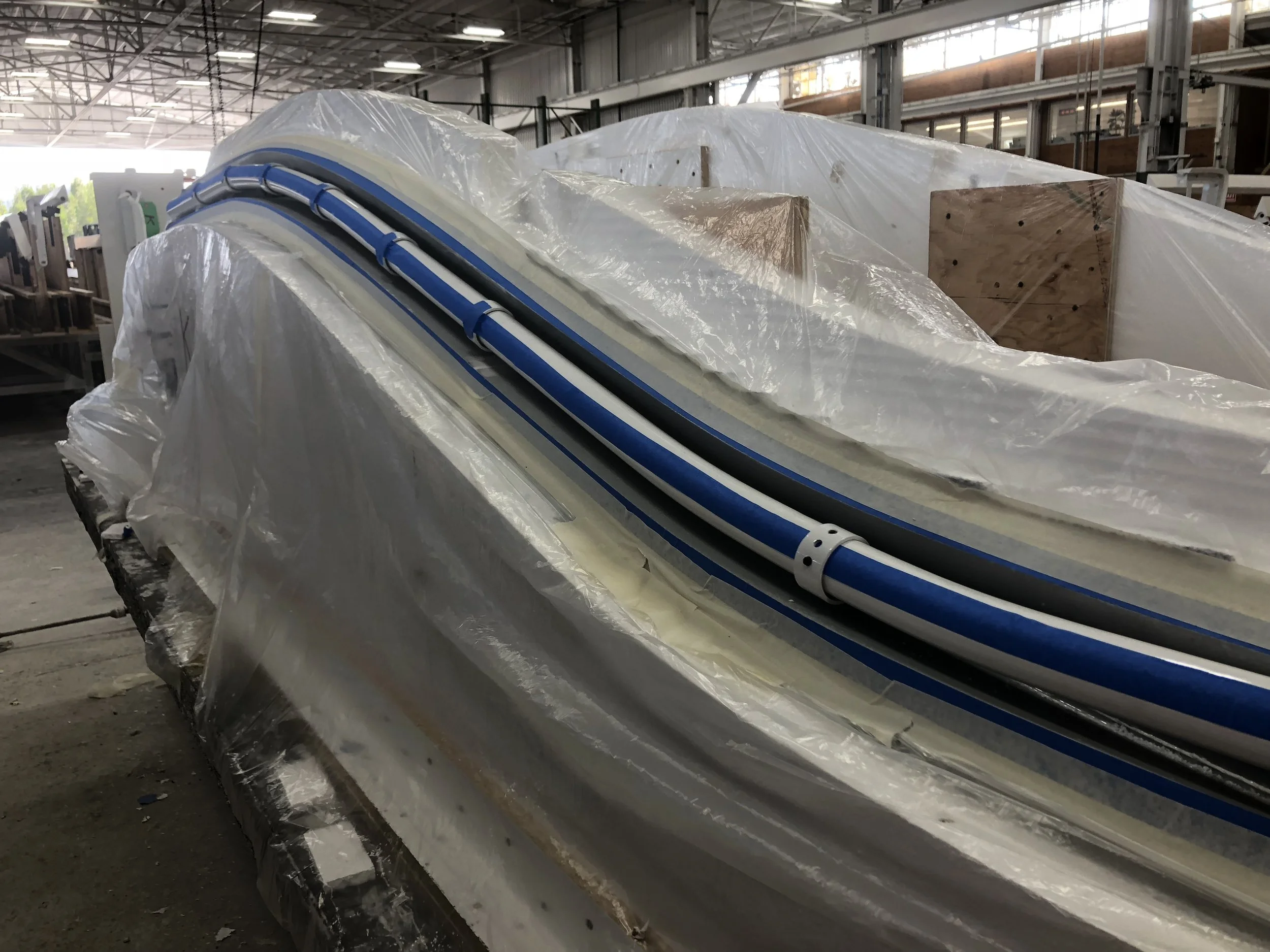 Unfinished airplane fuselage covered in plastic wrap inside an aircraft manufacturing facility.