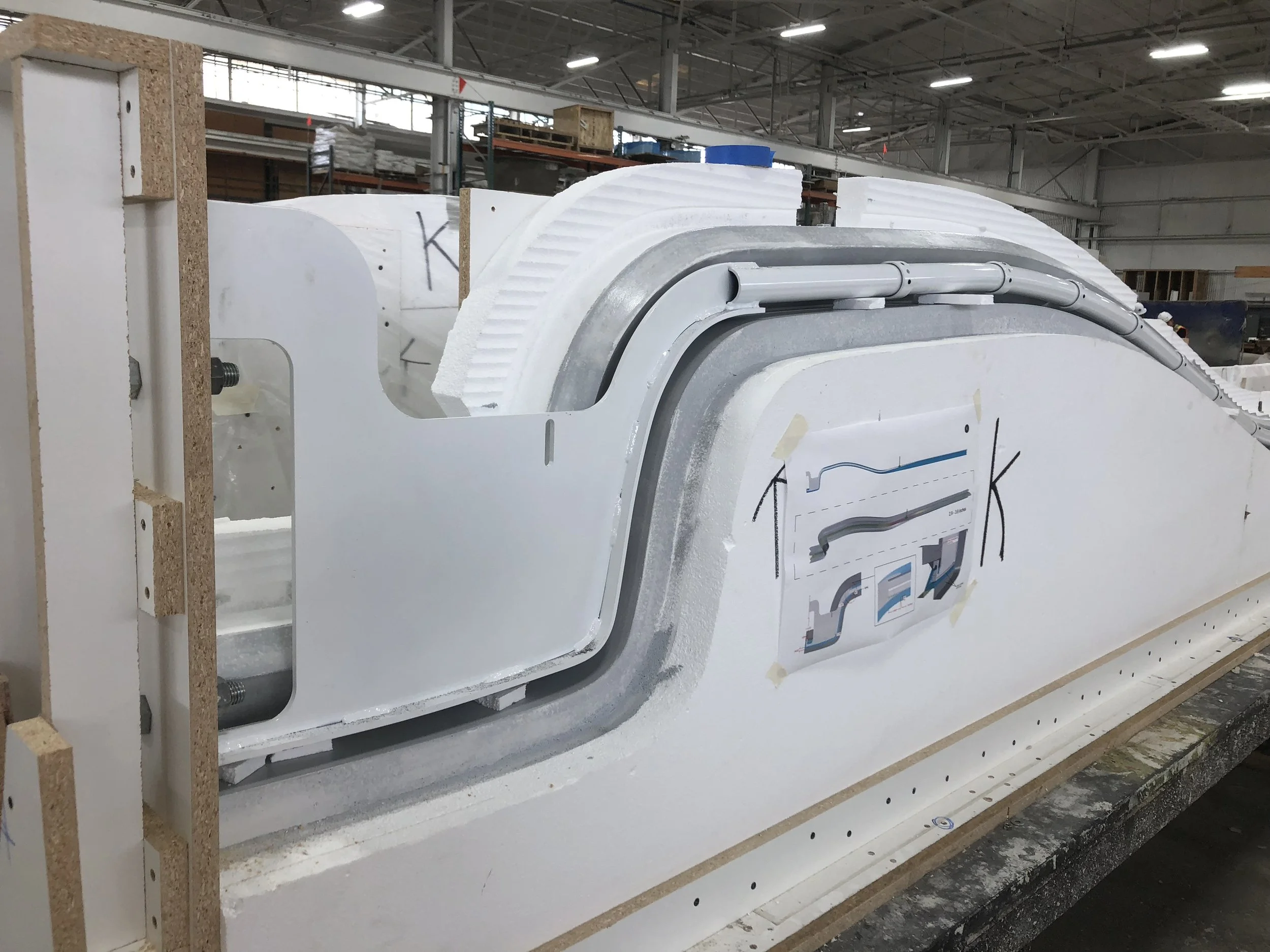 Construction of a large wind turbine blade, with parts assembled on a factory floor, including insulation foam and structural components.