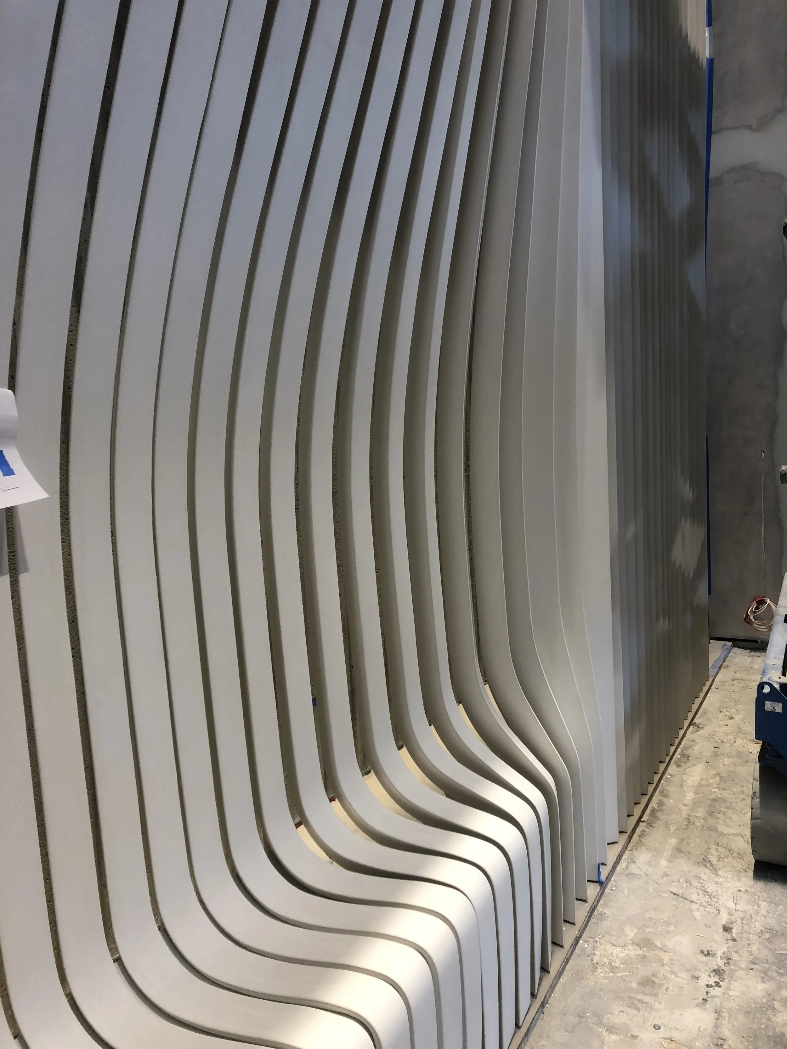 Multiple white curved architectural or furniture pieces standing vertically, arranged in a row in a workshop or warehouse setting.