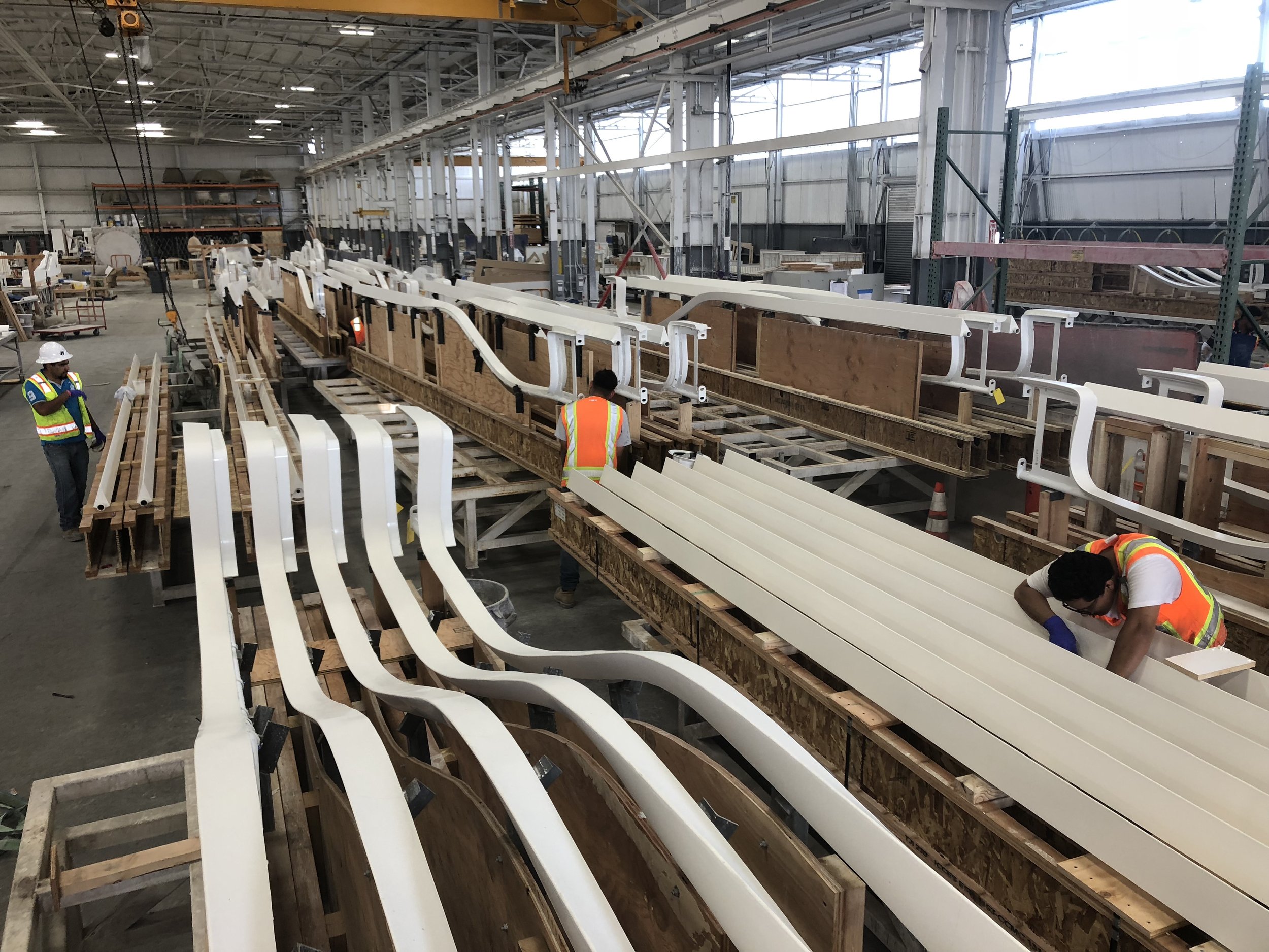 Construction workers inspecting large white structural components inside a factory or warehouse during manufacturing or assembly process.