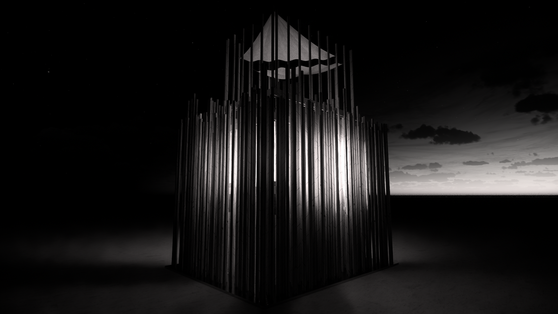 Nighttime photograph of a modern art sculpture made of vertical metal rods, with a geometric shape on top, illuminated from behind, against a cloudy sky and open landscape.