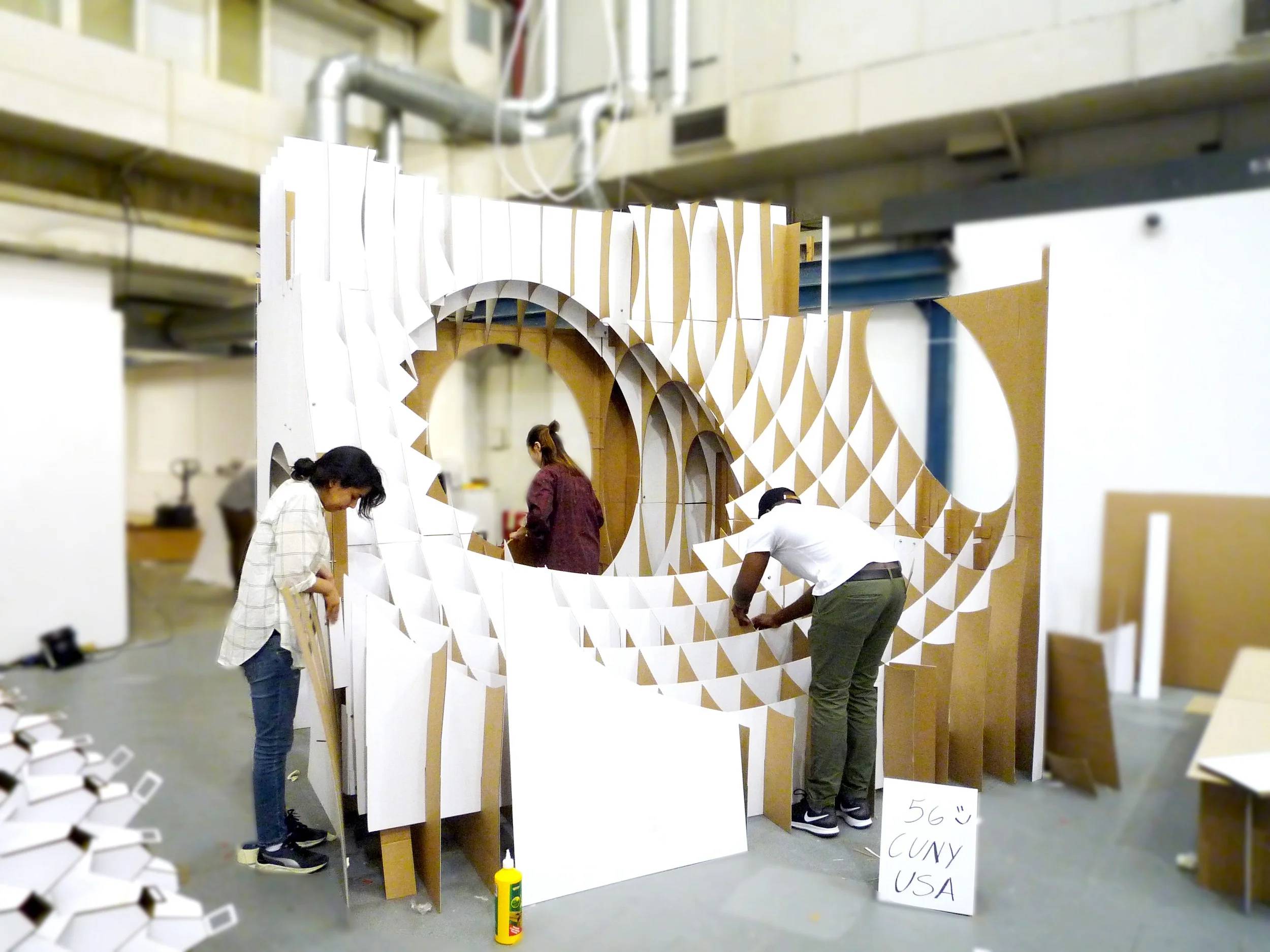 People assembling a large, decorative, wave-like partition made of white and tan geometric panels in an indoor space.