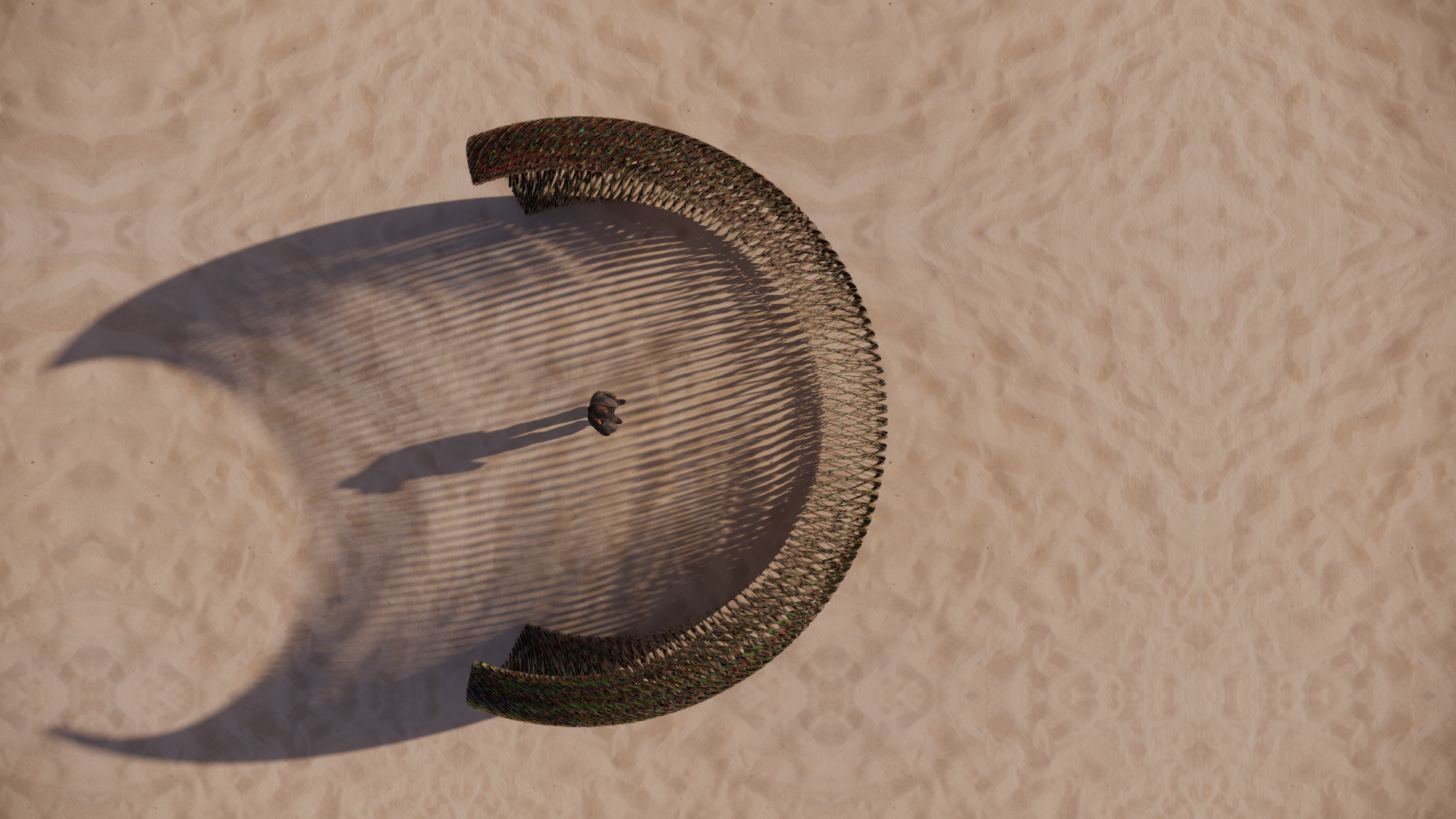 A person standing inside a circular sand sculpture with a lattice-like wall casting a long shadow on the sand.