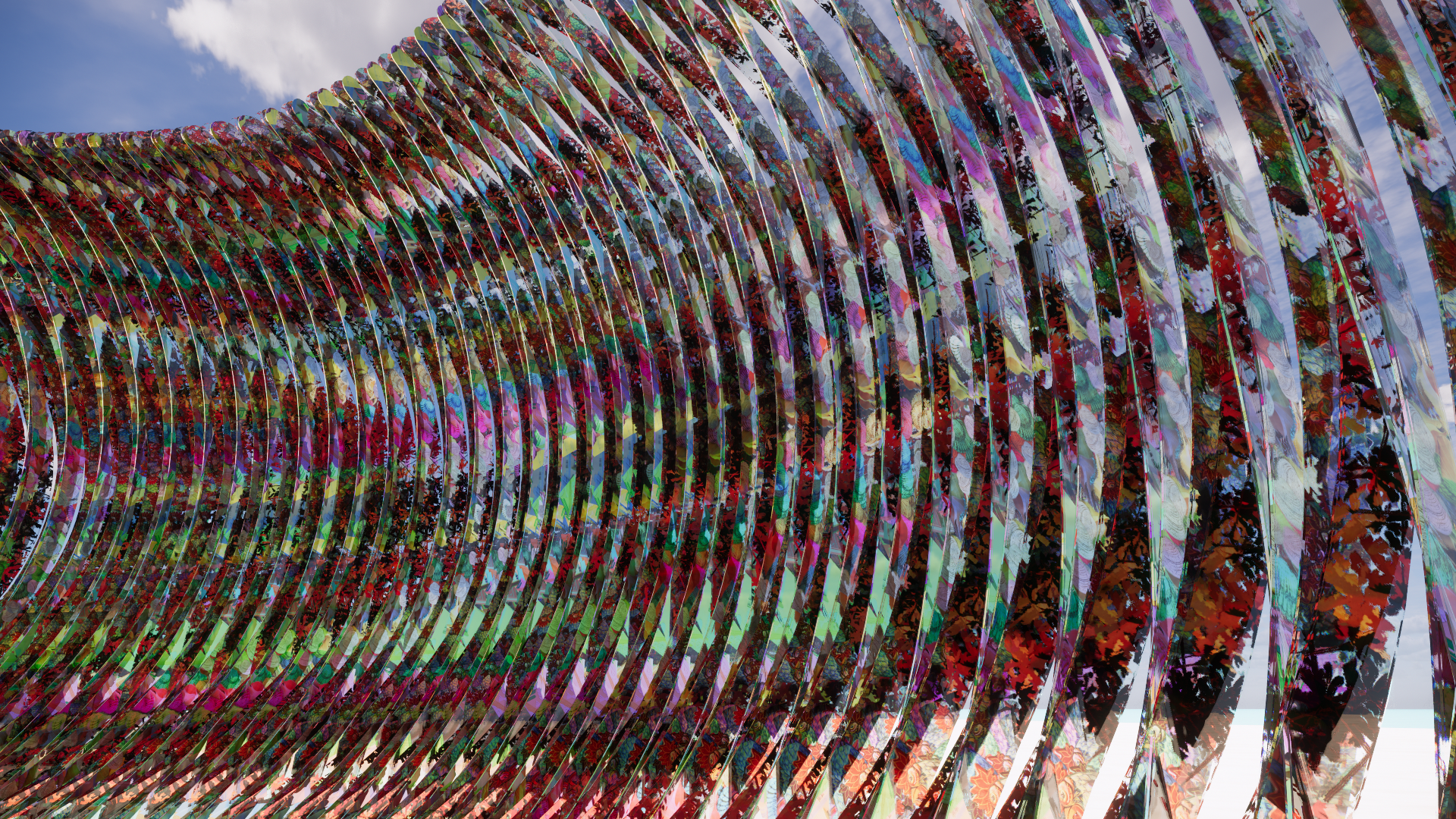 A large, modern sculpture made of colorful, reflective, curved metal strips arranged in a wave pattern against a blue sky with some white clouds.
