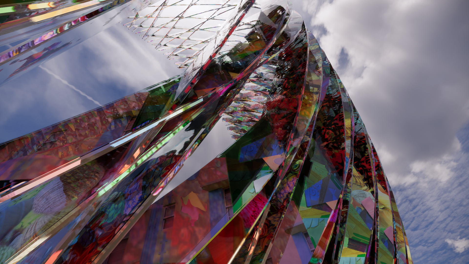 A colorful, reflective, abstract sculpture made of curved, intertwined metallic and glass-like ribbons, set against a cloudy sky.