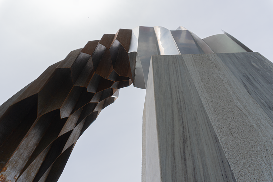 Close-up view of a modern sculpture with a combination of geometric and abstract shapes, made of metal and stone, taken from a low angle against a gray sky.