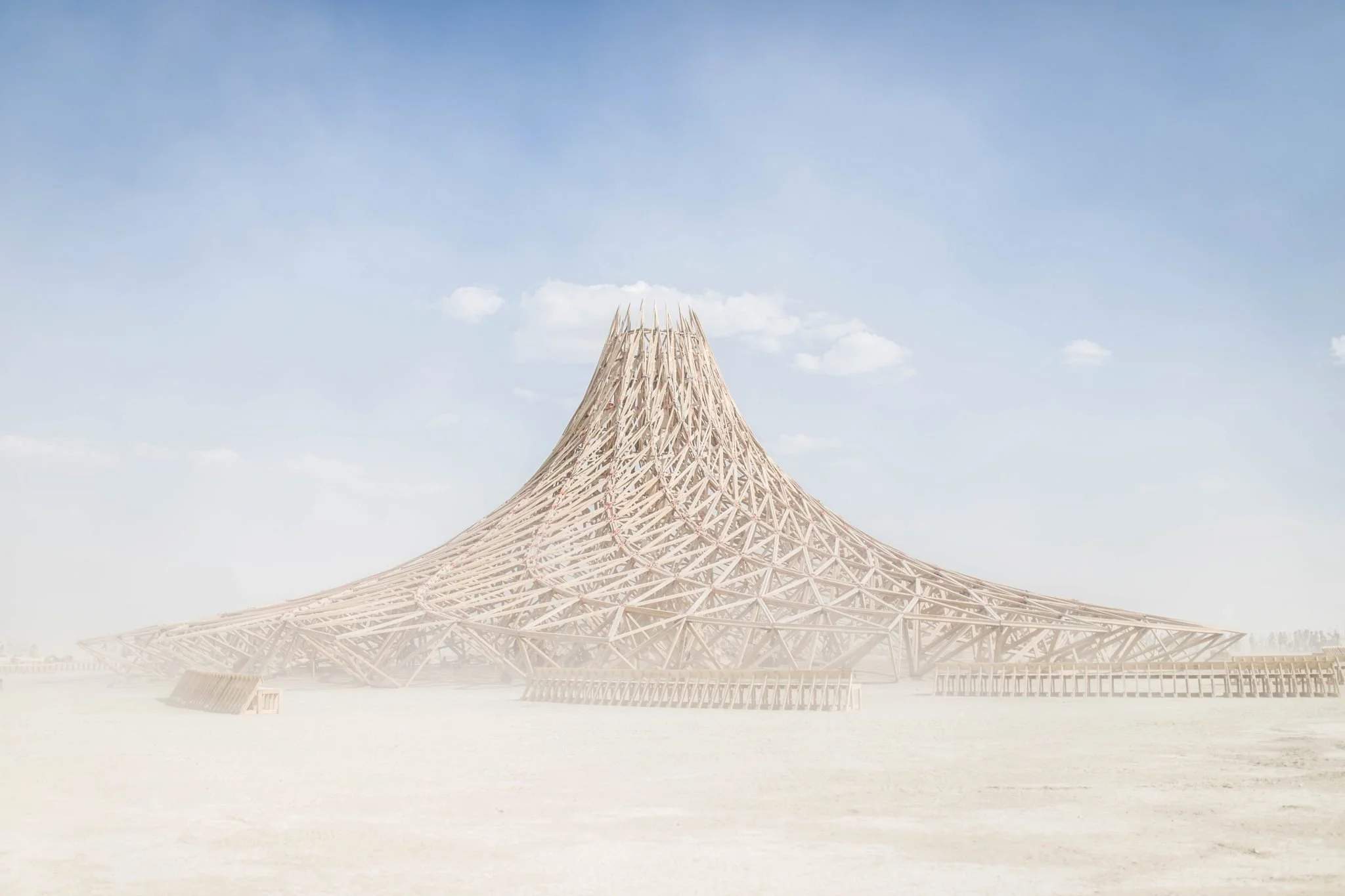 A large, modern wooden structure with a cone shape, resembling a mountain or volcano, set against a blue sky with a few white clouds.