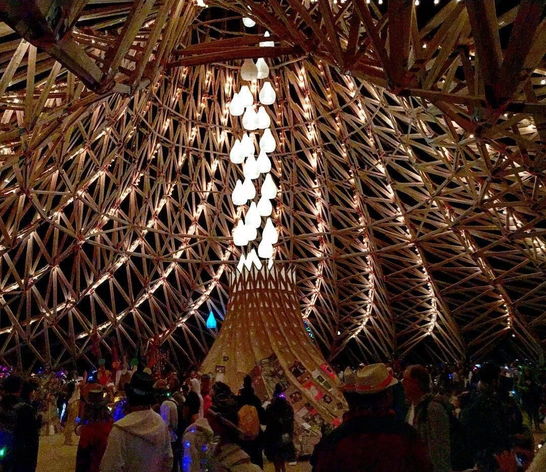 Interior of a large wooden dome with hanging lights and a crowd of people.