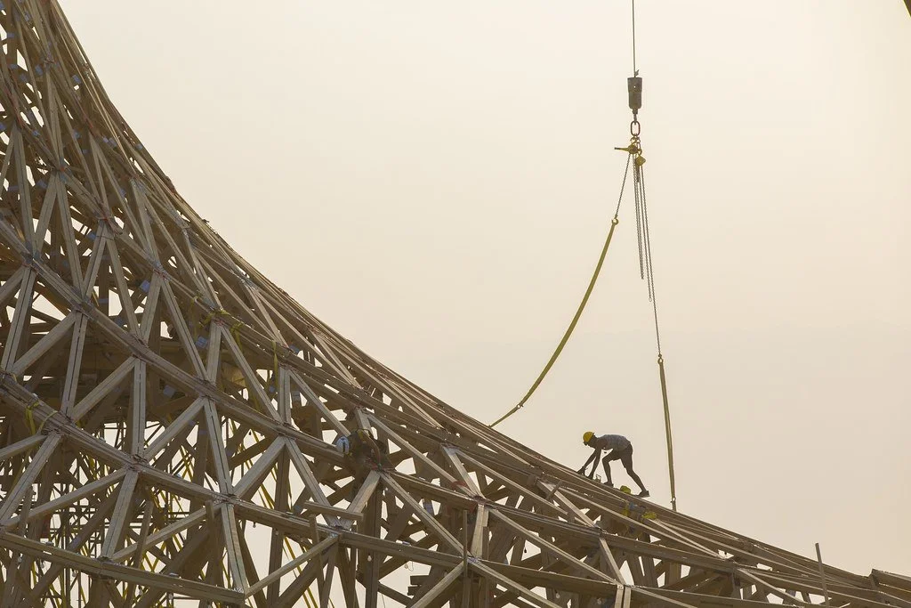 Workers installing a large steel structure on a high crane at a construction site.