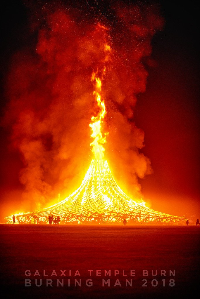 Large bonfire resembling a temple on fire at night with people standing around it