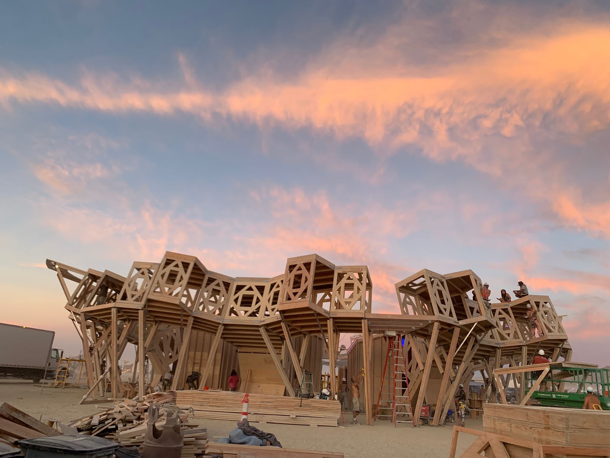 Wooden structure under construction against a sunset sky with pink and orange clouds.