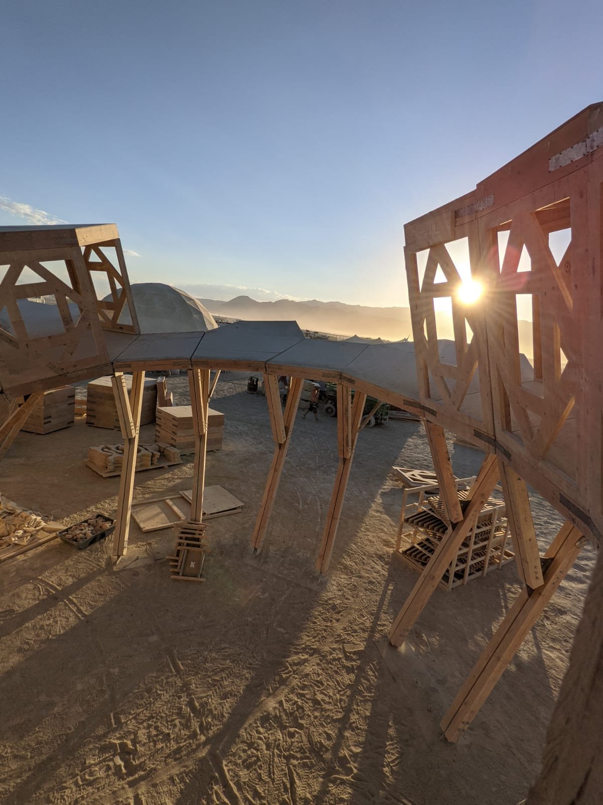 Wooden construction framework at sunrise or sunset in a desert landscape with mountains in the background.