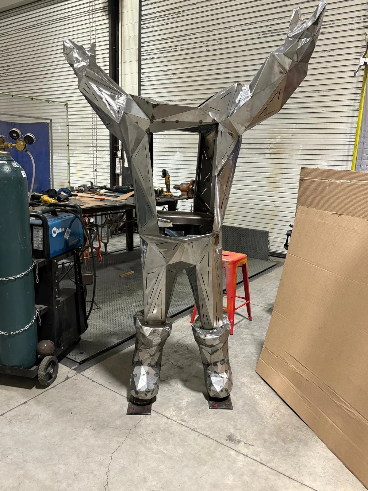 A metallic sculpture of a deer standing inside a garage or workshop surrounded by tools and equipment.