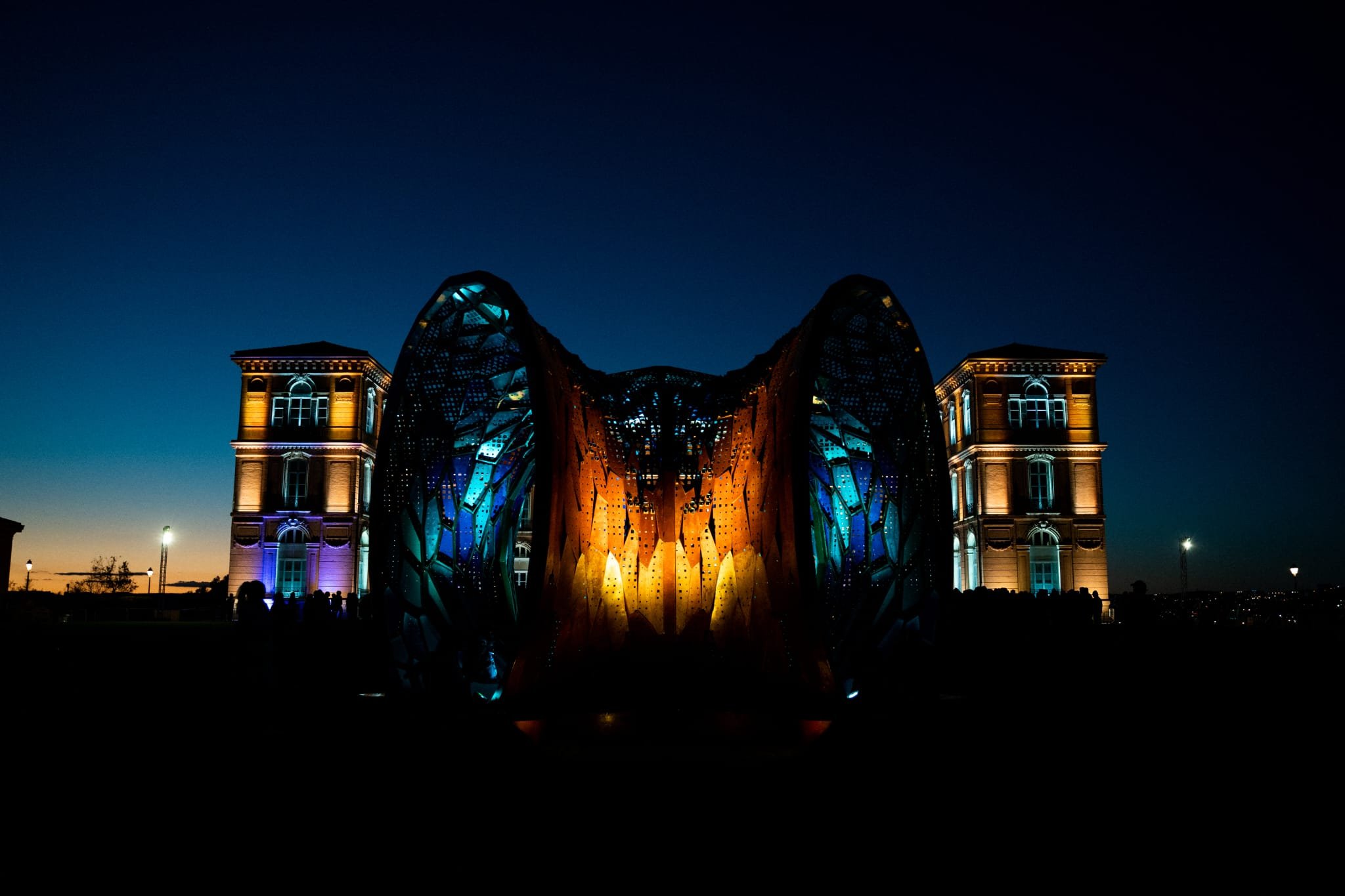 Night view of the Leeds Castle in London illuminated with colorful lights, showcasing its historic architecture and a modern art installation in the foreground.