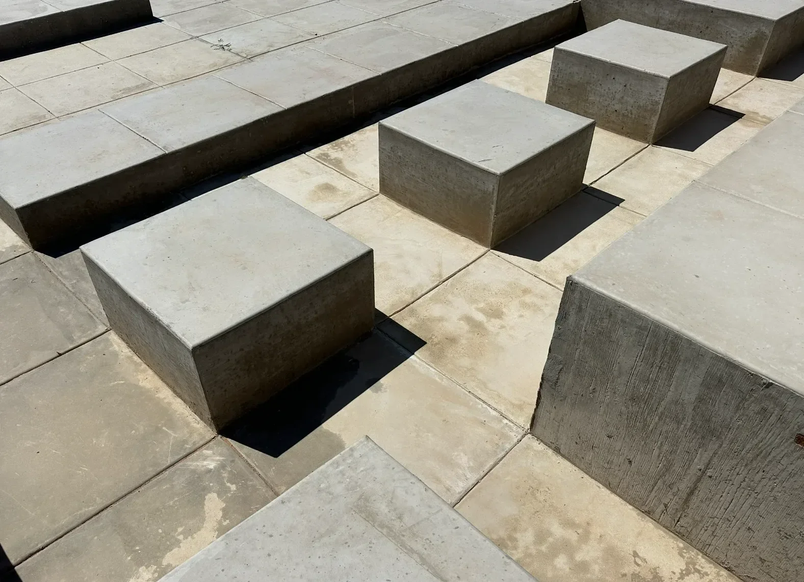 A series of concrete steps and blocks arranged on a tiled surface, with shadows cast by the objects.
