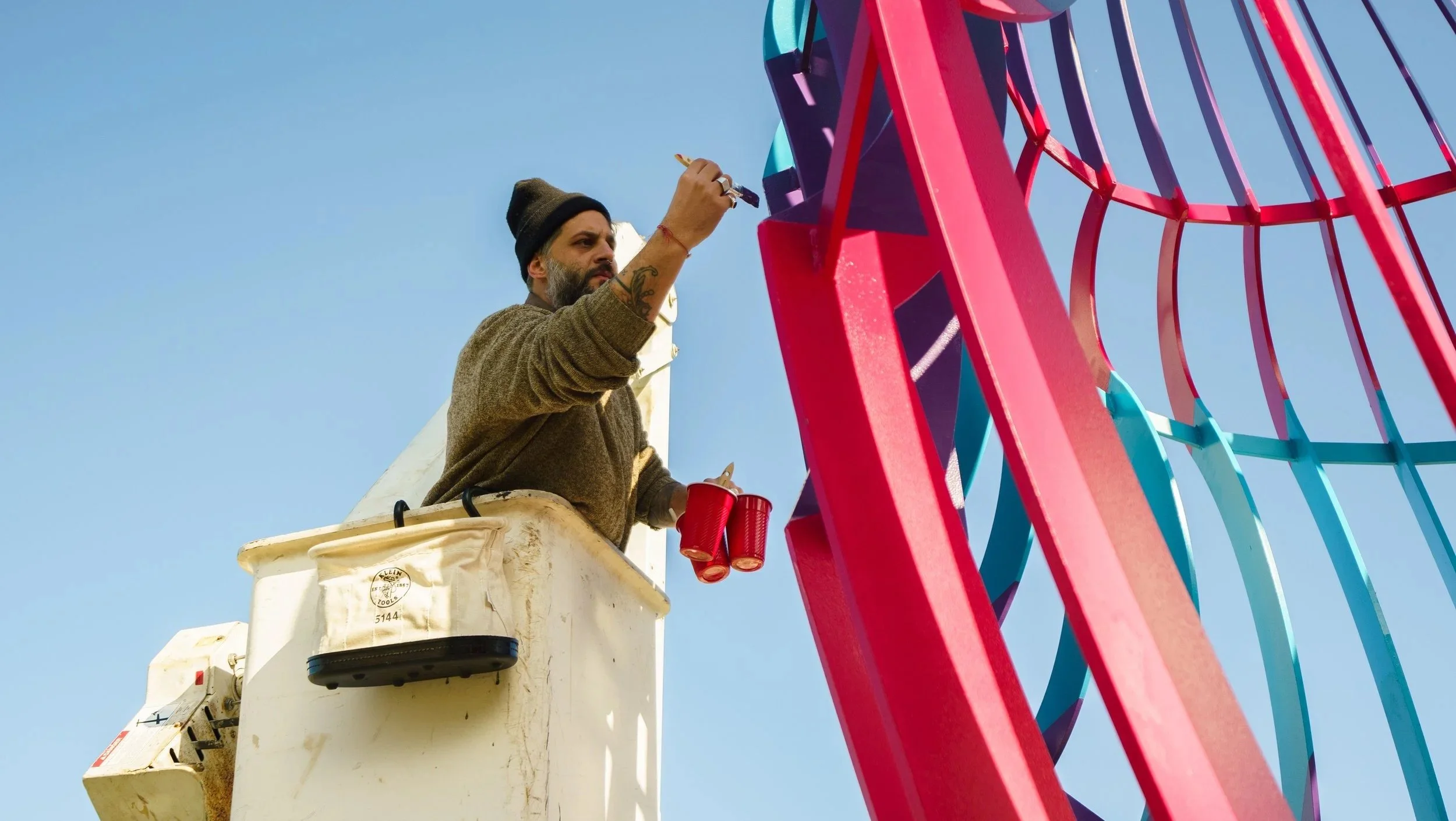 A man working on a colorful Ferris wheel from a bucket lift.