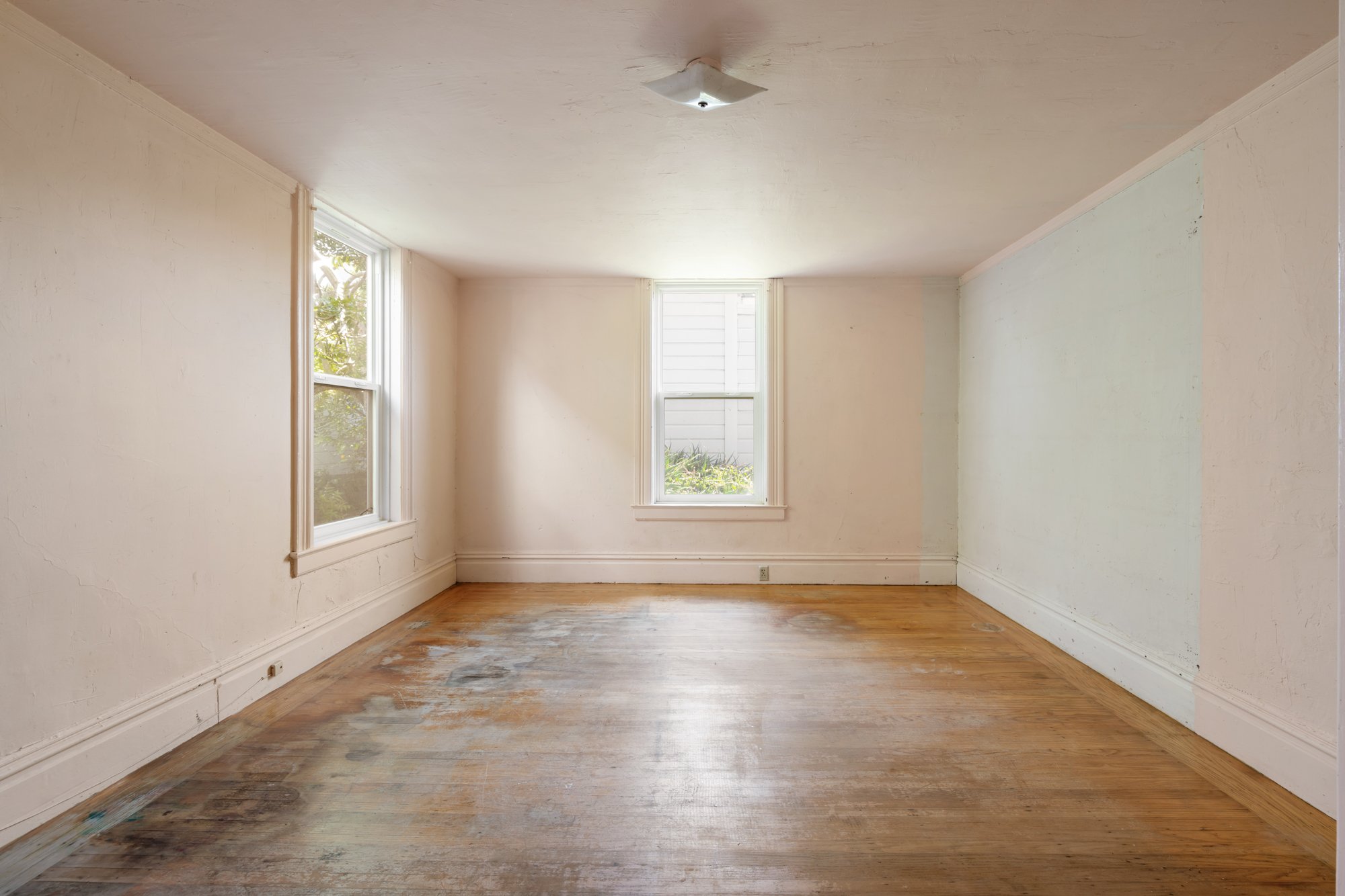 Empty room with three windows, white walls, hardwood floor, and a ceiling light fixture.