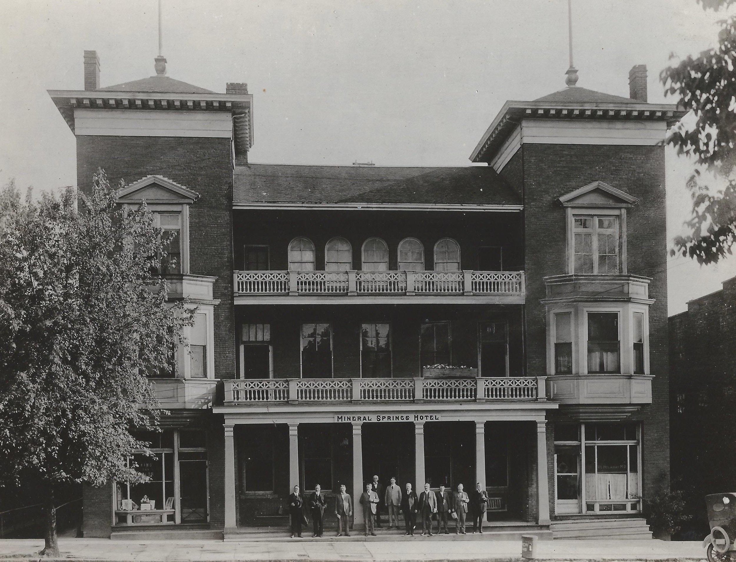 Black and white photograph of the Mineral Springs Hotel with a group of people standing on the front steps.