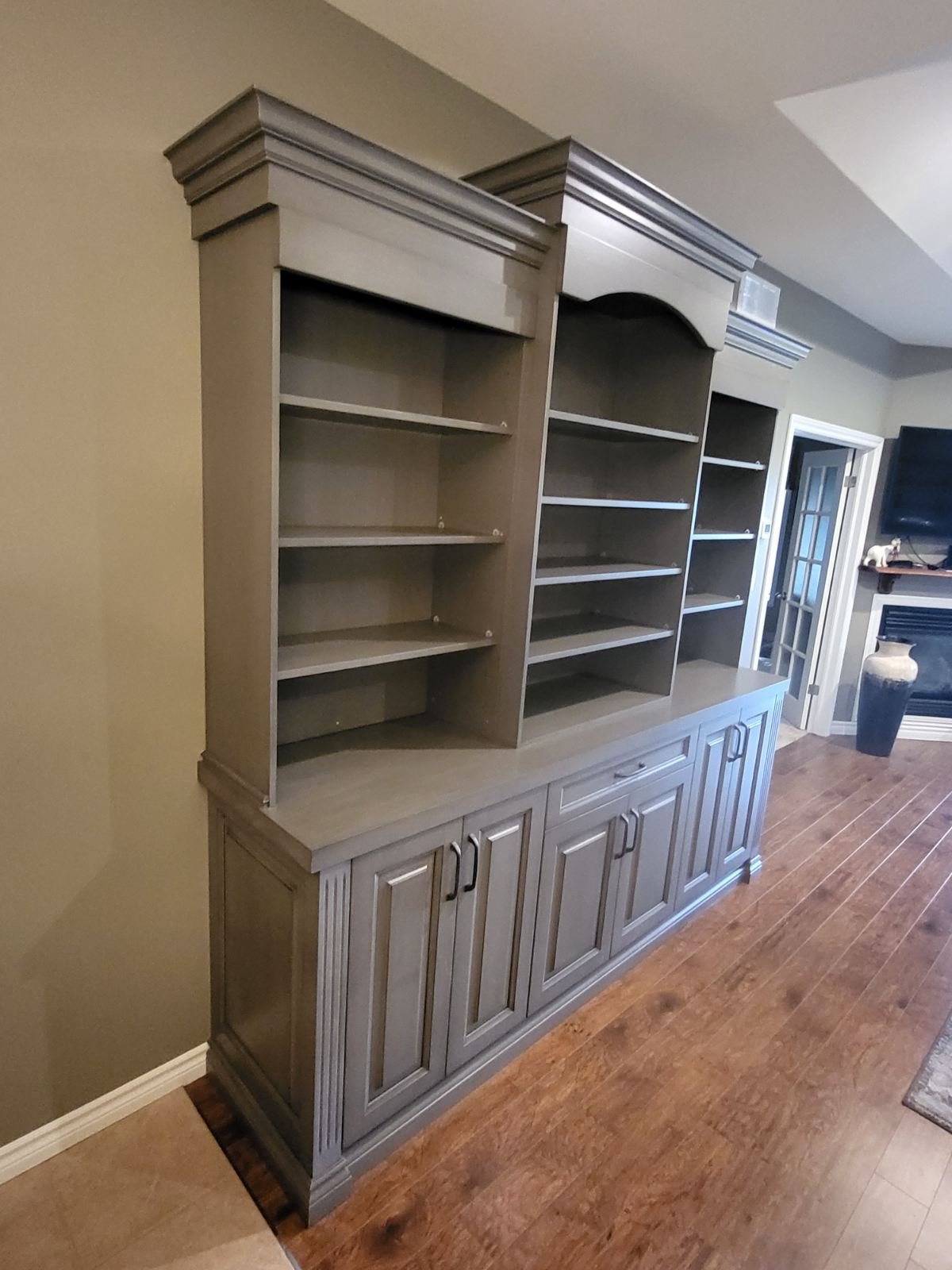 custom built bookshelf with three side bye side sections ofopen upper shelves and lower cabinet doors, crown moulding for detail along the top finished in light grey