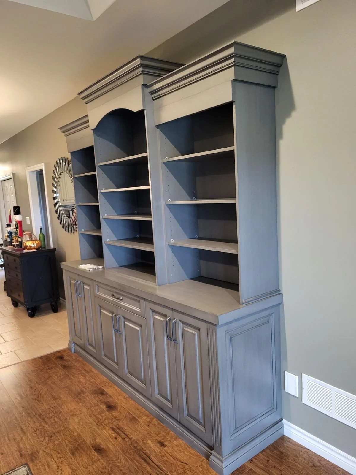 custom built bookshelf with three side bye side sections ofopen upper shelves and lower cabinet doors, crown moulding for detail along the top finished in light grey