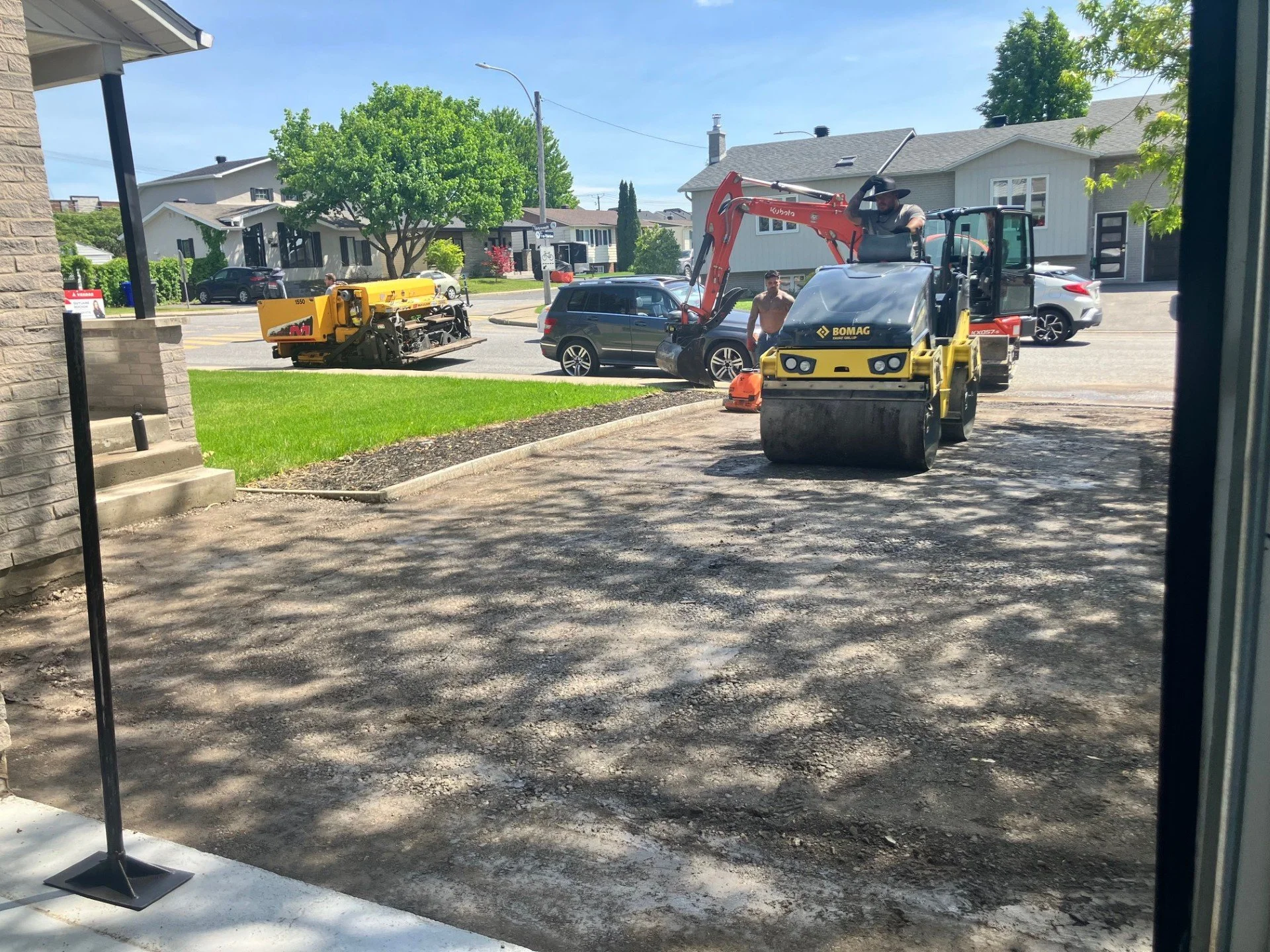 Travaux de construction de voirie dans une zone résidentielle, avec des machines, des ouvriers et des maisons en arrière-plan.