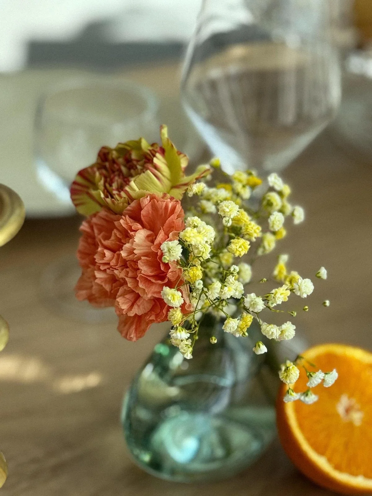 Un bouquet de fleurs dans un vase en verre, comprenant une carnation rose, des petites fleurs blanches et une autre fleur avec des pétales vert, dans un environnement intérieur.