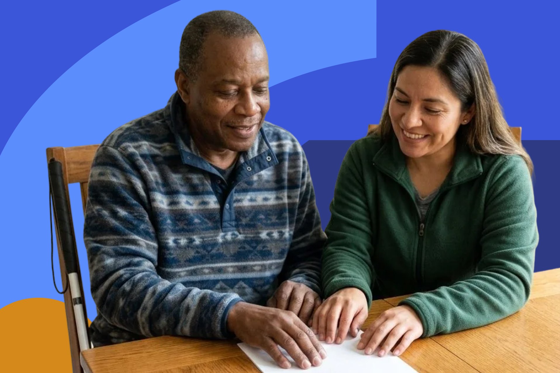 A man using a white cane and a woman review a housing document together at a table.