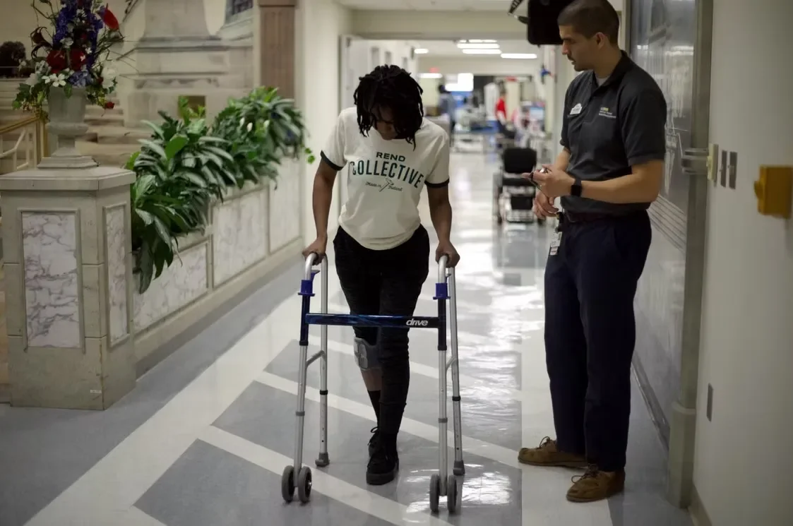 Tyree using walker at medical facility with medical professional nearby