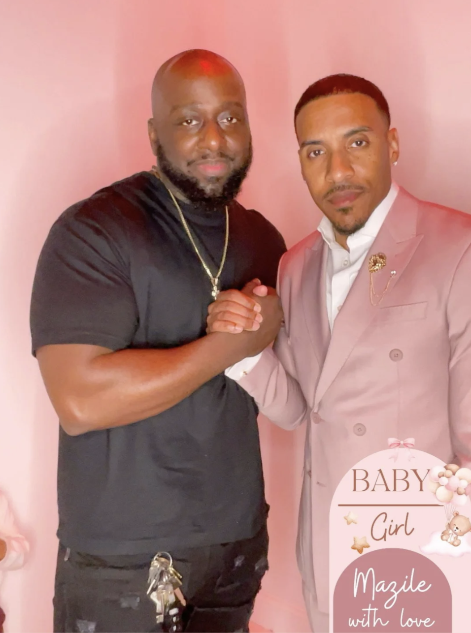Two men shaking hands and posing for a photo against a pink background. One man is wearing a black shirt and accessories, the other a light pink suit with a brooch. A decorative baby girl-themed graphic in the bottom right corner reads "BABY Girl, Ma