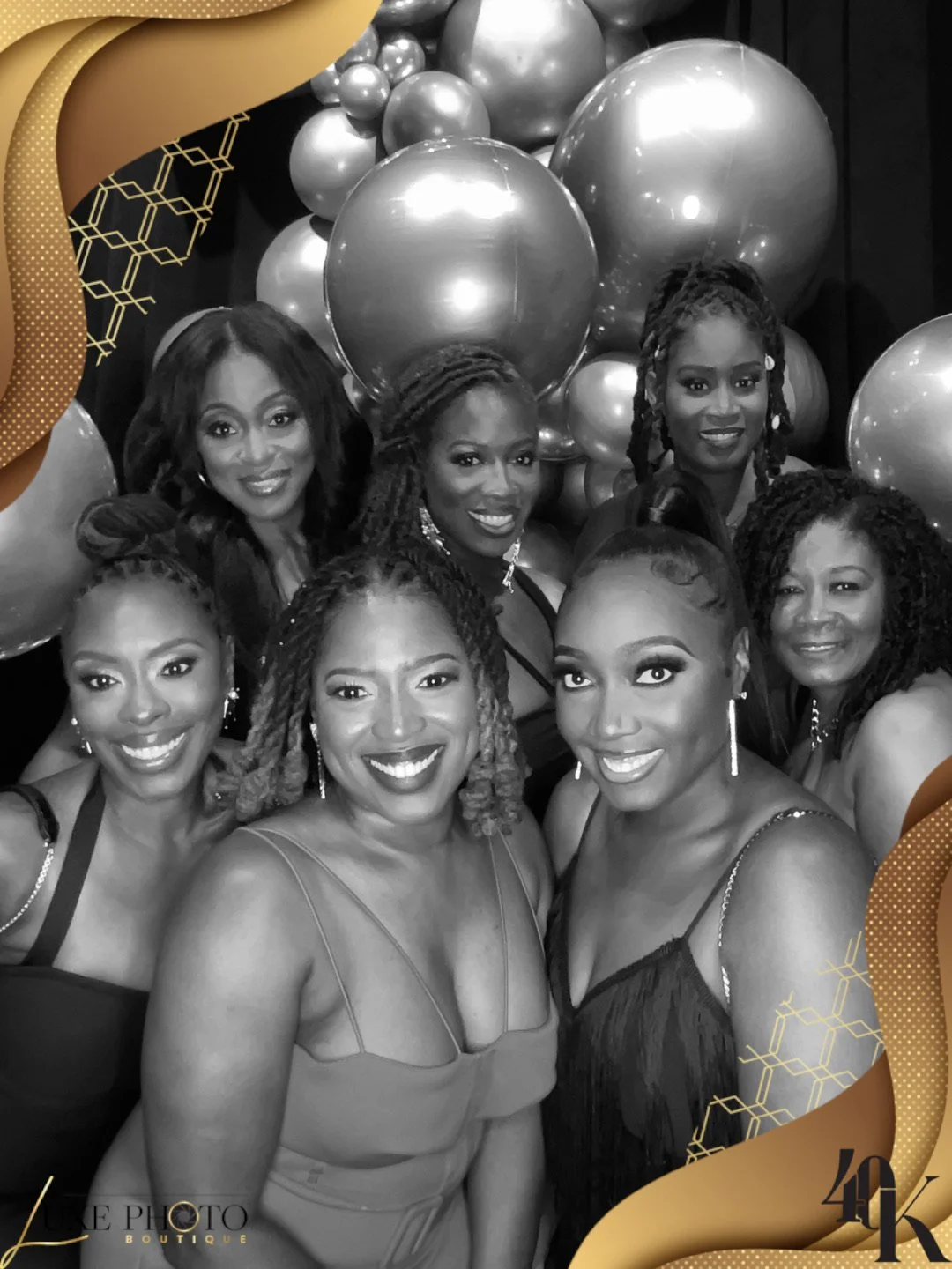 Group of women dressed in formal attire at a celebration, with a backdrop of balloons, in black and white.