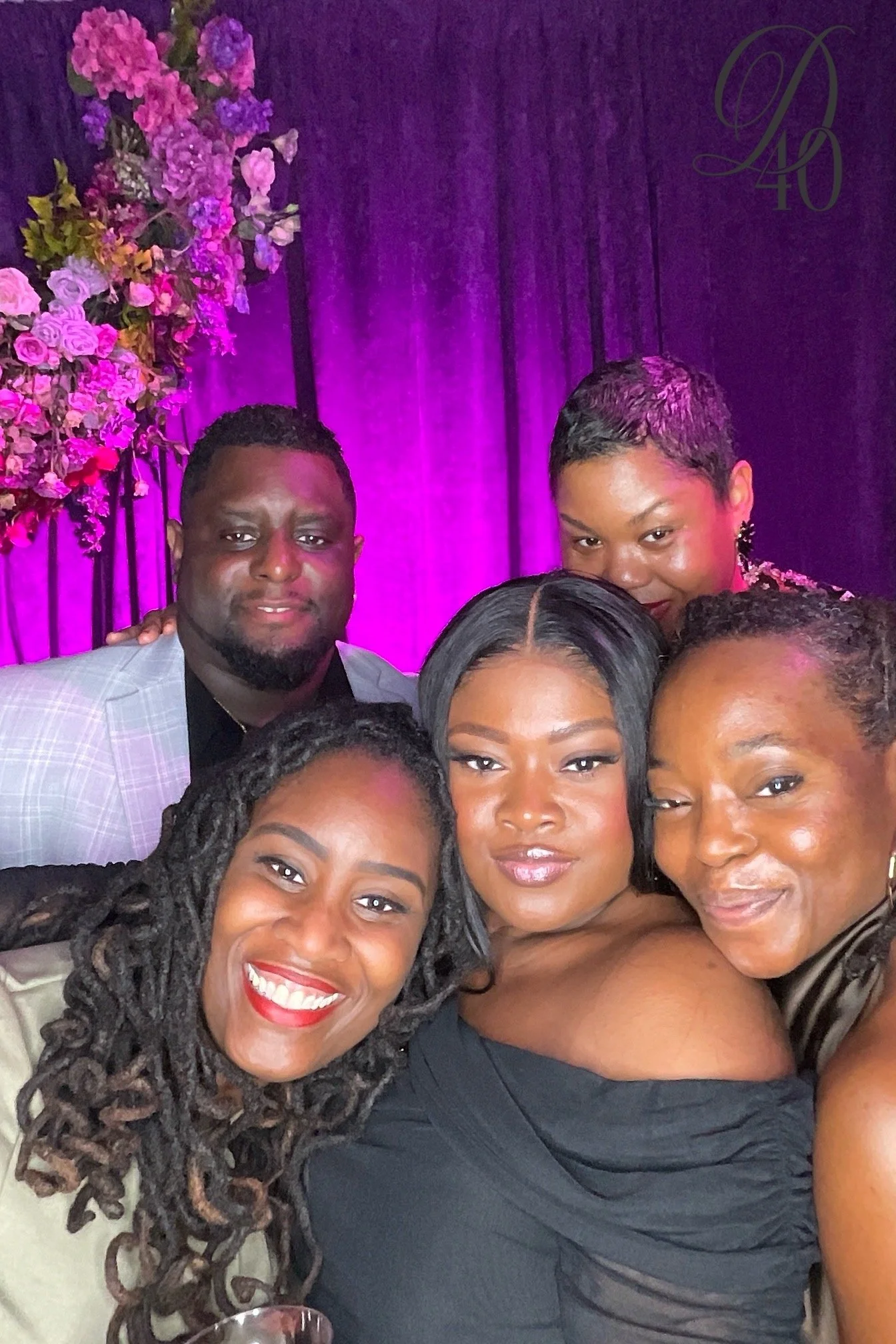 Group of people taking a selfie at an event with purple lighting and floral decorations in the background.