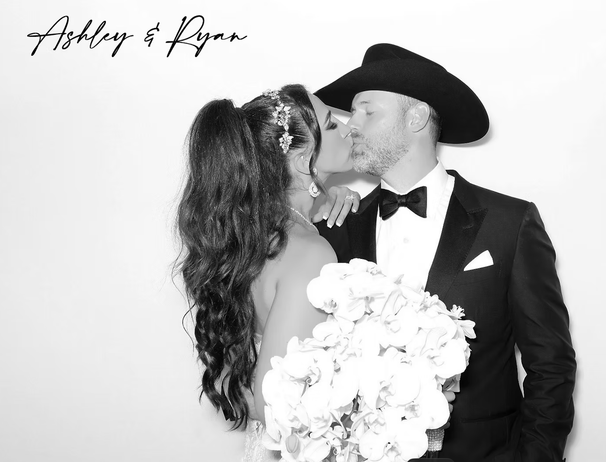 Black and white photo of a bride and groom sharing a kiss, with the bride holding a large bouquet of flowers, and the groom wearing a tuxedo with a bow tie and a cowboy hat. The names Ashley and Ryan are written in cursive in the upper left corner.
