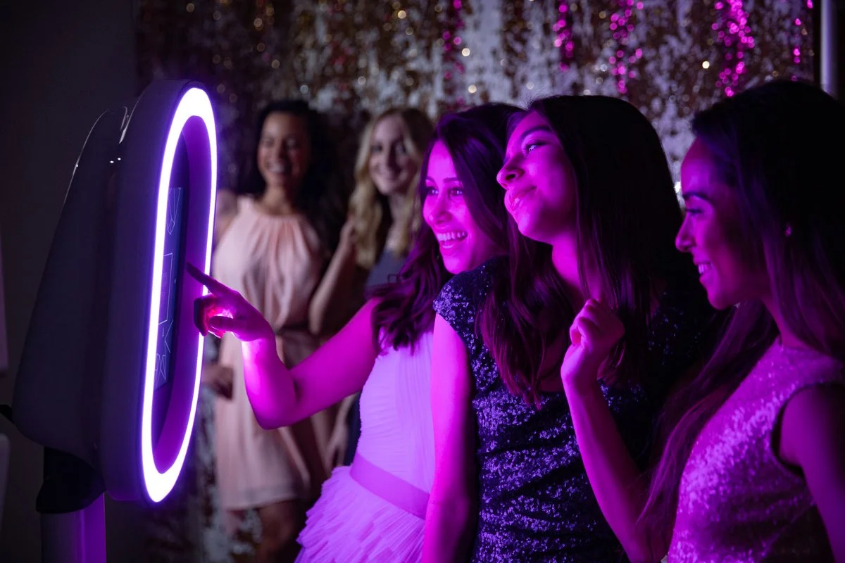 Four women at a party having fun using a photo booth with neon lights, smiling, and enjoying the moment.