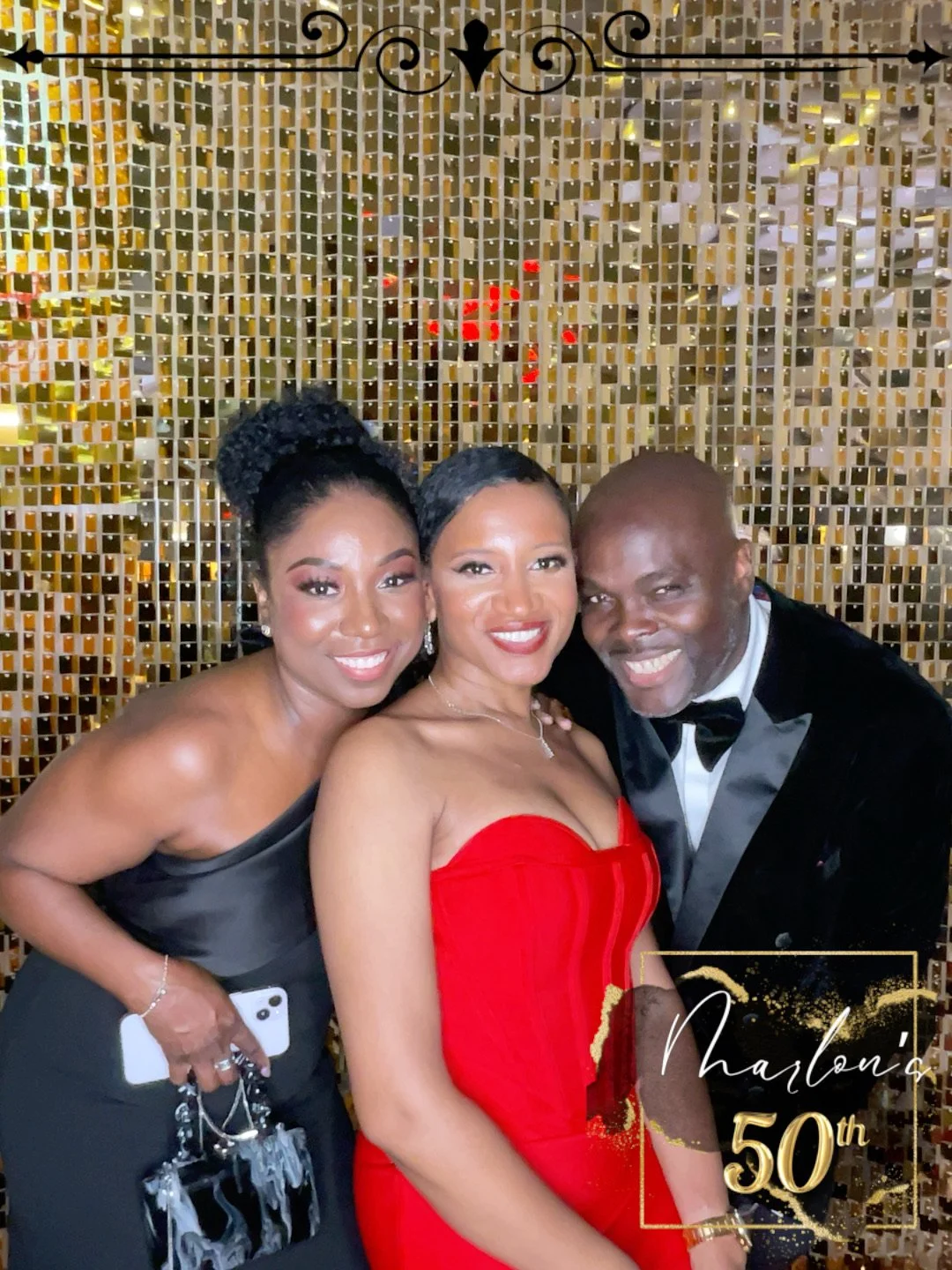 Three people dressed in formal attire posing for a photo in front of a gold mosaic wall, celebrating Marlon's 50th birthday.