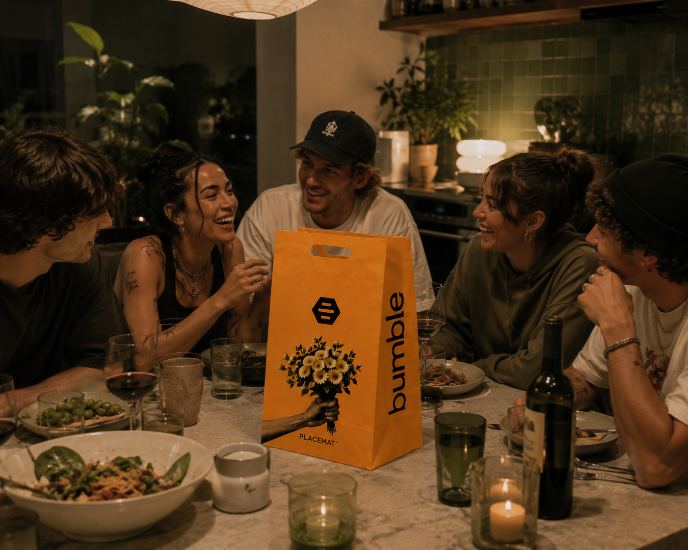 Group of six friends sitting around a dining table enjoying a meal and laughing at night.