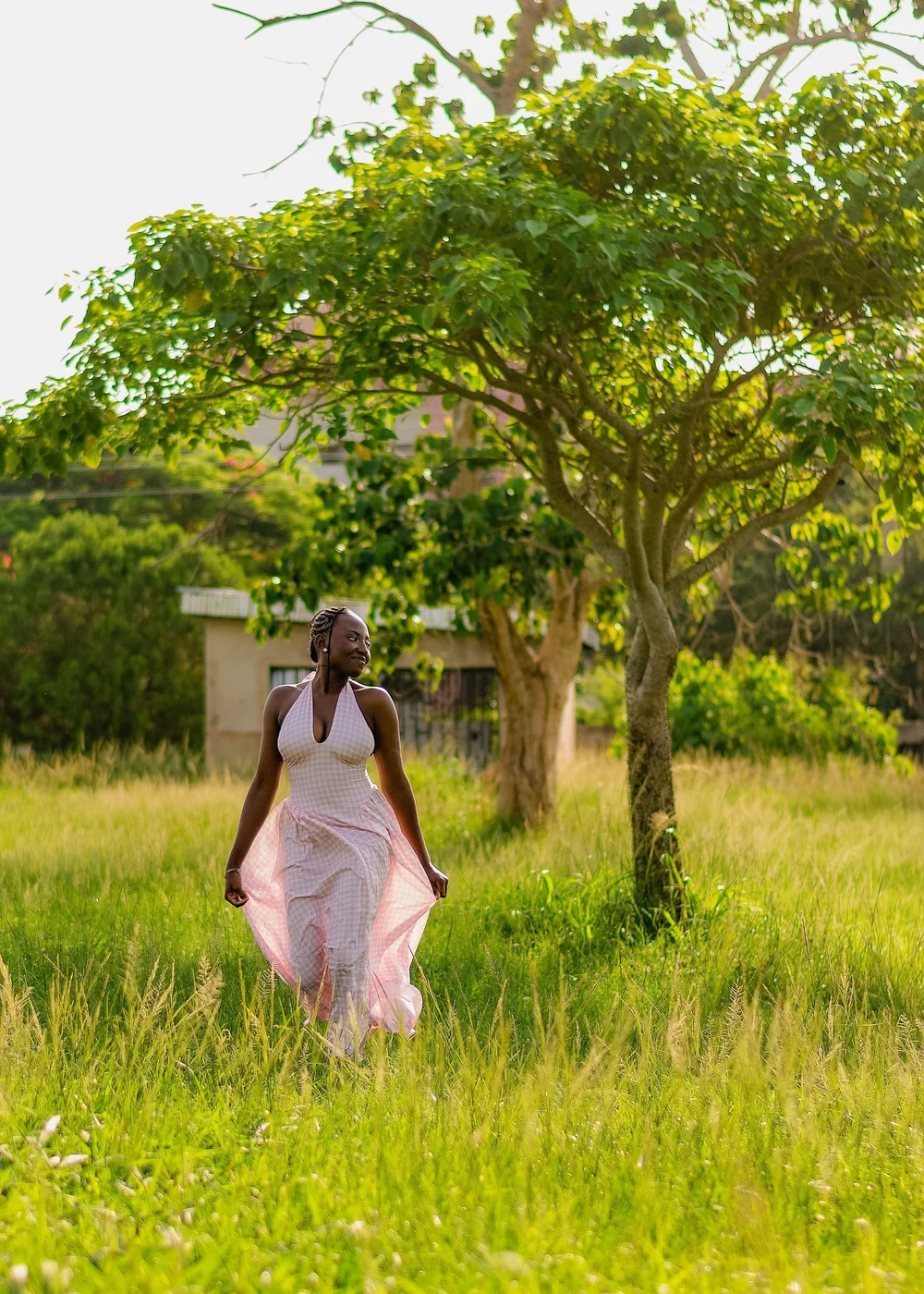 A woman in a pink gingham dress twirling under a tree