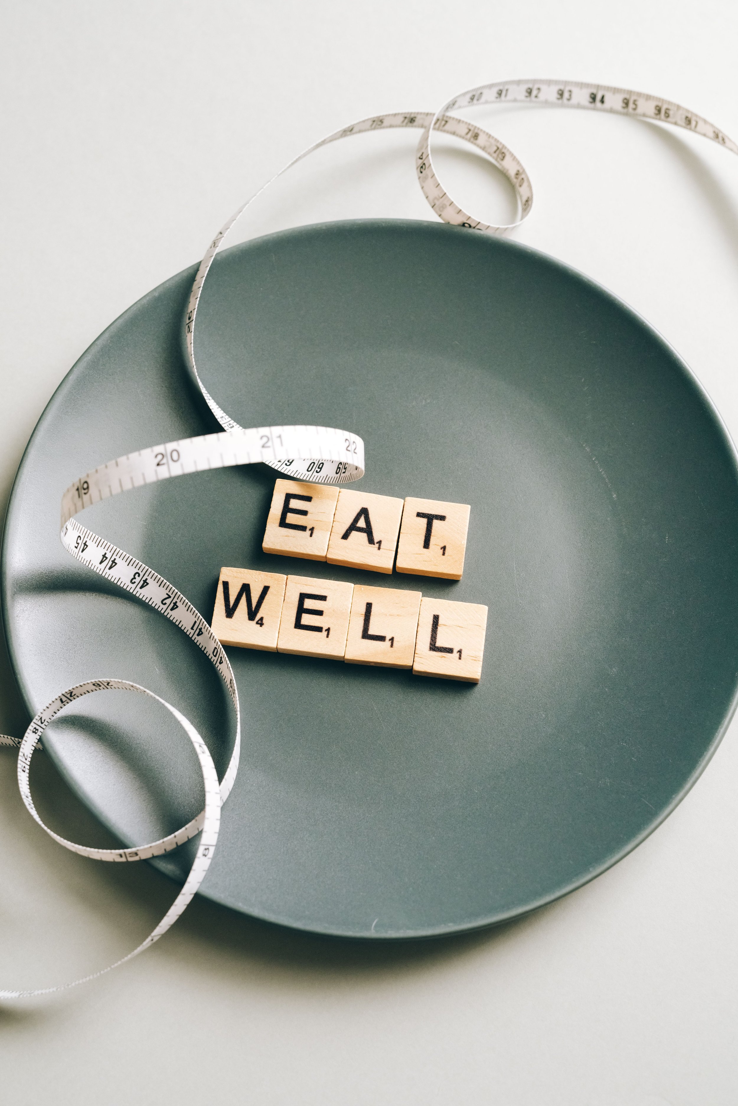 A measuring tape curled on a plate beside letter tiles that spell eat well