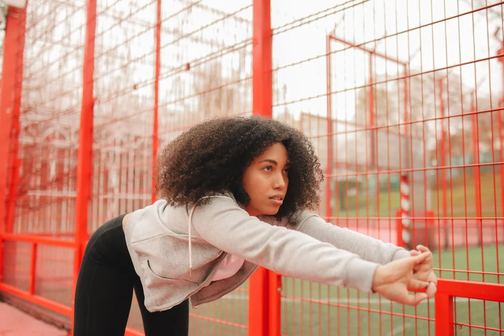 A woman stretching beside a red fence