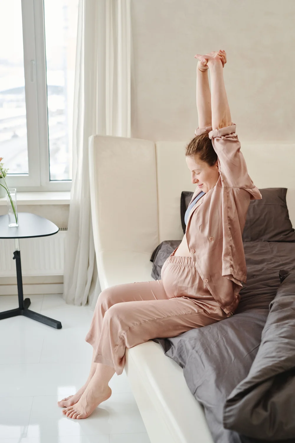 A pregnant woman stretching in soft pink loungewear