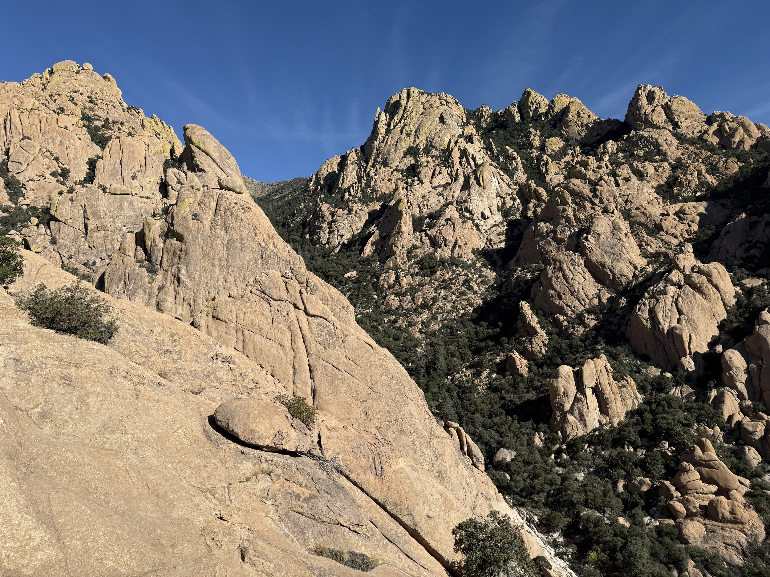 A rugged mountain range with large, beige-colored rocks and sparse vegetation under a clear blue sky.