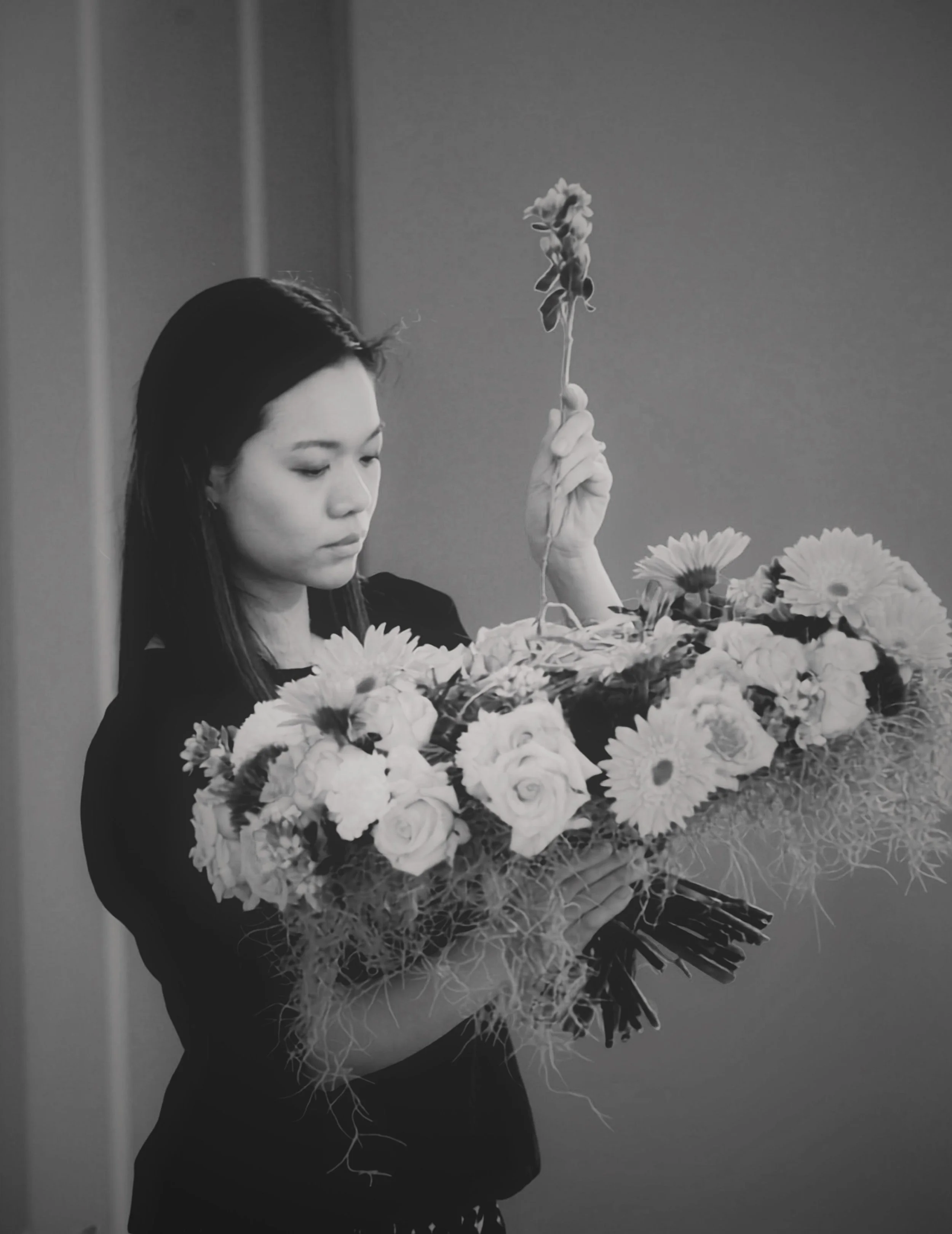 A candid black and white portrait of The Artist from USÉKI, deeply focused while creating a contemporary Sogetsu Ikebana flower arrangement in a minimalist studio setting.