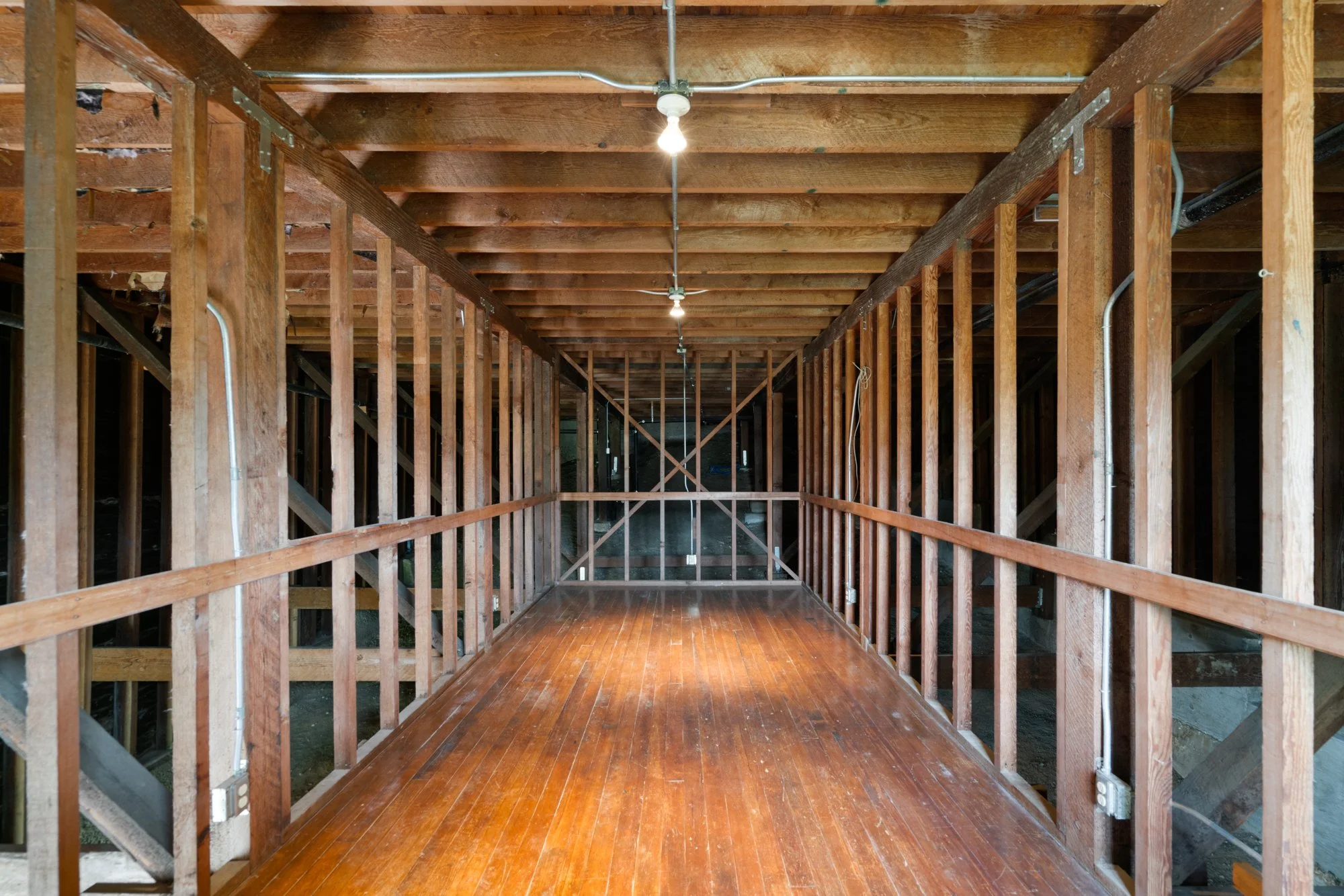 The image shows the interior of a building under construction, with exposed wooden framing, electrical wiring, and unfinished flooring.