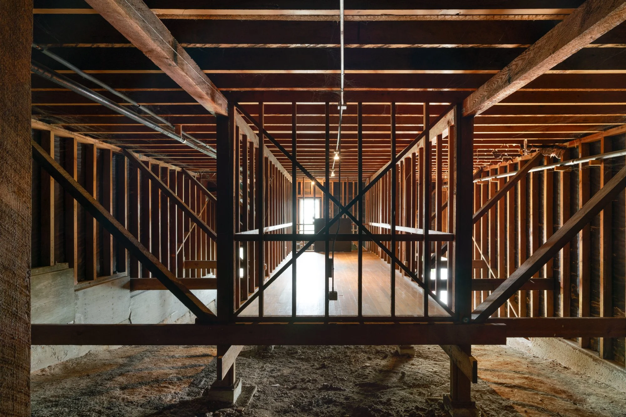 Interior view of a building under construction with exposed wooden framing and support beams, with a doorway leading to natural light.
