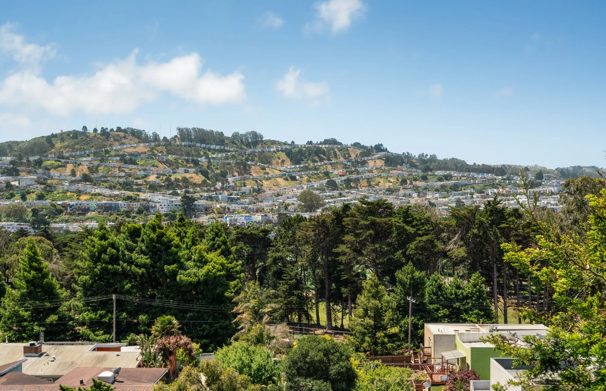 A hillside filled with colorful houses and greenery under a blue sky with scattered clouds.